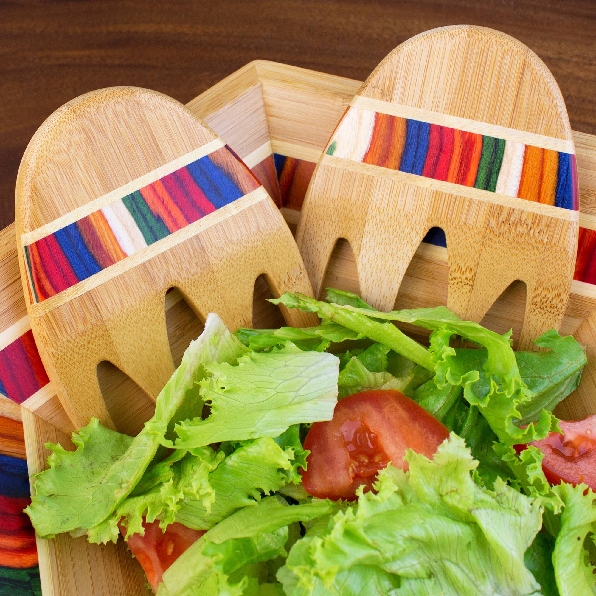 A wooden bowl with green salad and tomato slices is served with Marrakesh Collection Salad Hands, featuring colorful stripes.