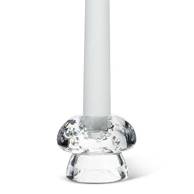 A white candle stands upright in the Mushroom Glass Taper Candle Holder, which measures 2" tall by 2.5" in diameter and features a rounded, textured base inspired by mushroom decor.