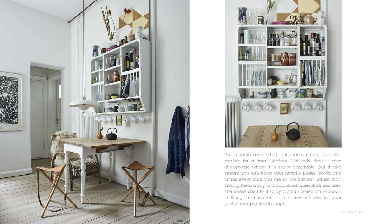 A small kitchen features a wooden table, folding chairs, and a wall shelf with dishes, all bathed in natural light—reflecting the style found in Scandinavian Home Interiors Inspired by Light by Niki Brantmark.