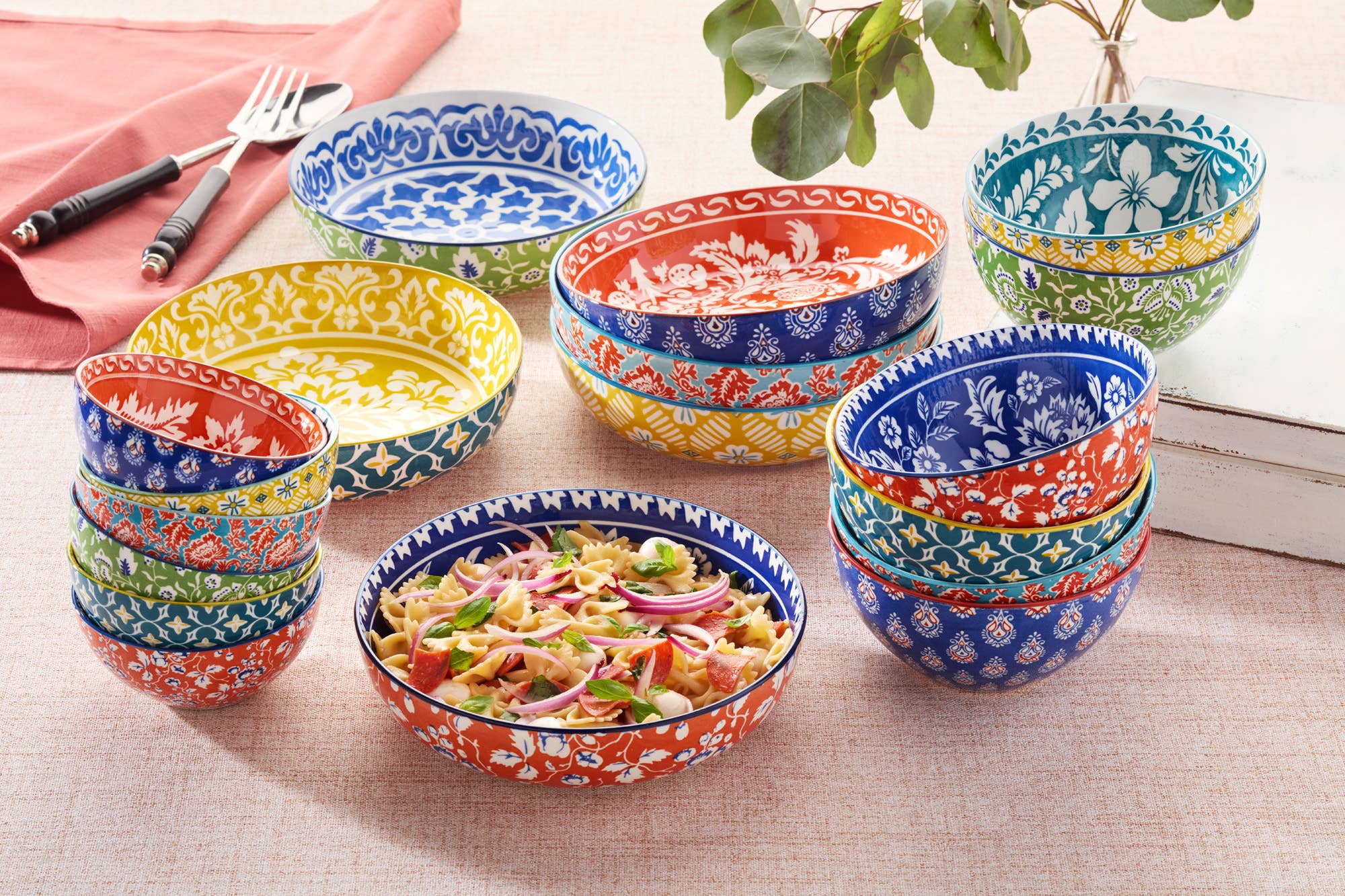 A set of Bowls: Multi-Color Patterned Porcelain All Purpose Bowl 6.25in 6 in vibrant colors, one filled with salad, displayed on a table alongside cutlery, a napkin, and a plant.