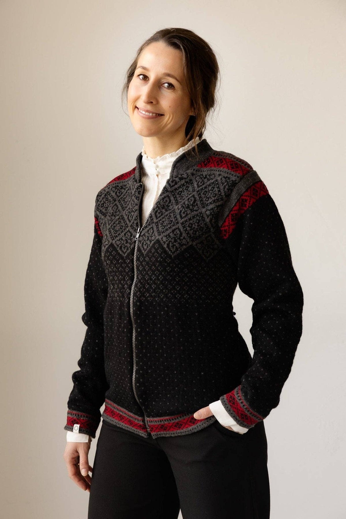 A person wearing a wool zip-front cardigan featuring red and grey Nordic patterns on the yoke and cuffs.