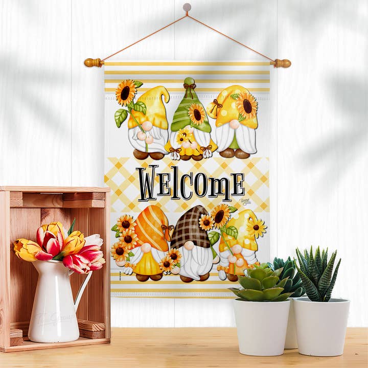 The Flag: Spring Gnomes Garden Floral Gnome Decor Flag, featuring cartoon gnomes, sunflowers, and WELCOME, is displayed above a wooden box of flowers and two small potted succulents.