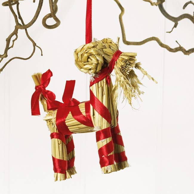 Scandinavian Julbock straw goat ornament wrapped in red ribbon with small bows.