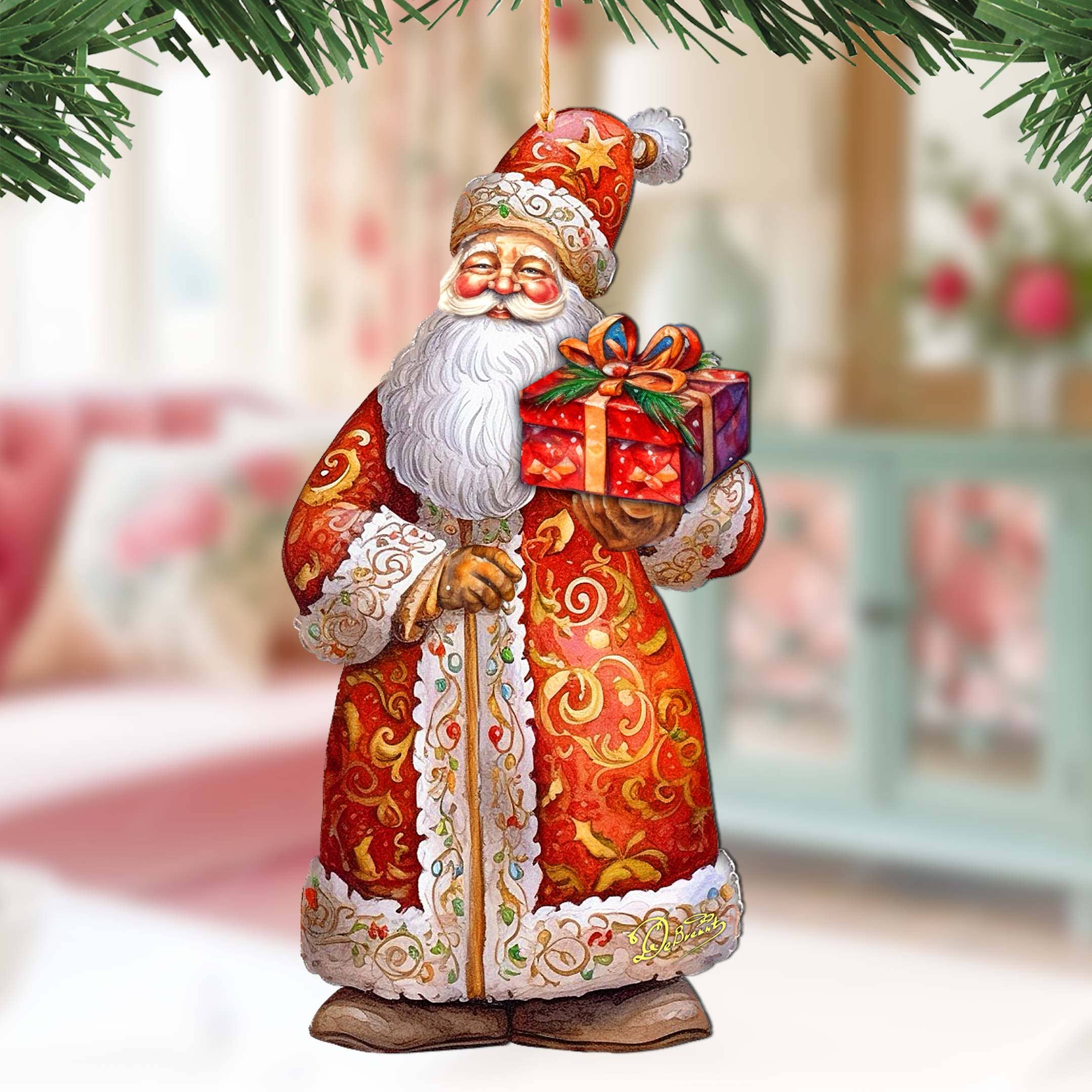 The St. Nick's Gift Wood Ornament by G Debrekht ("Christmas Santa") features Santa in a red ornate coat holding a wrapped gift, measures 5.5" tall by 3" wide, with festive decor and pine branches in the background.