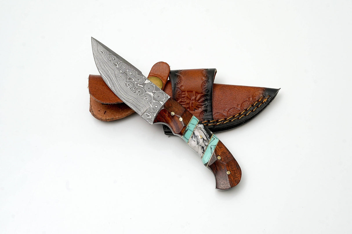 The Titan International Hand-Forged Damascus Steel Field Knife features a patterned blade and custom hybrid wood & turquoise handle, displayed on a brown leather sheath against a white background—premium outdoor utility gear.