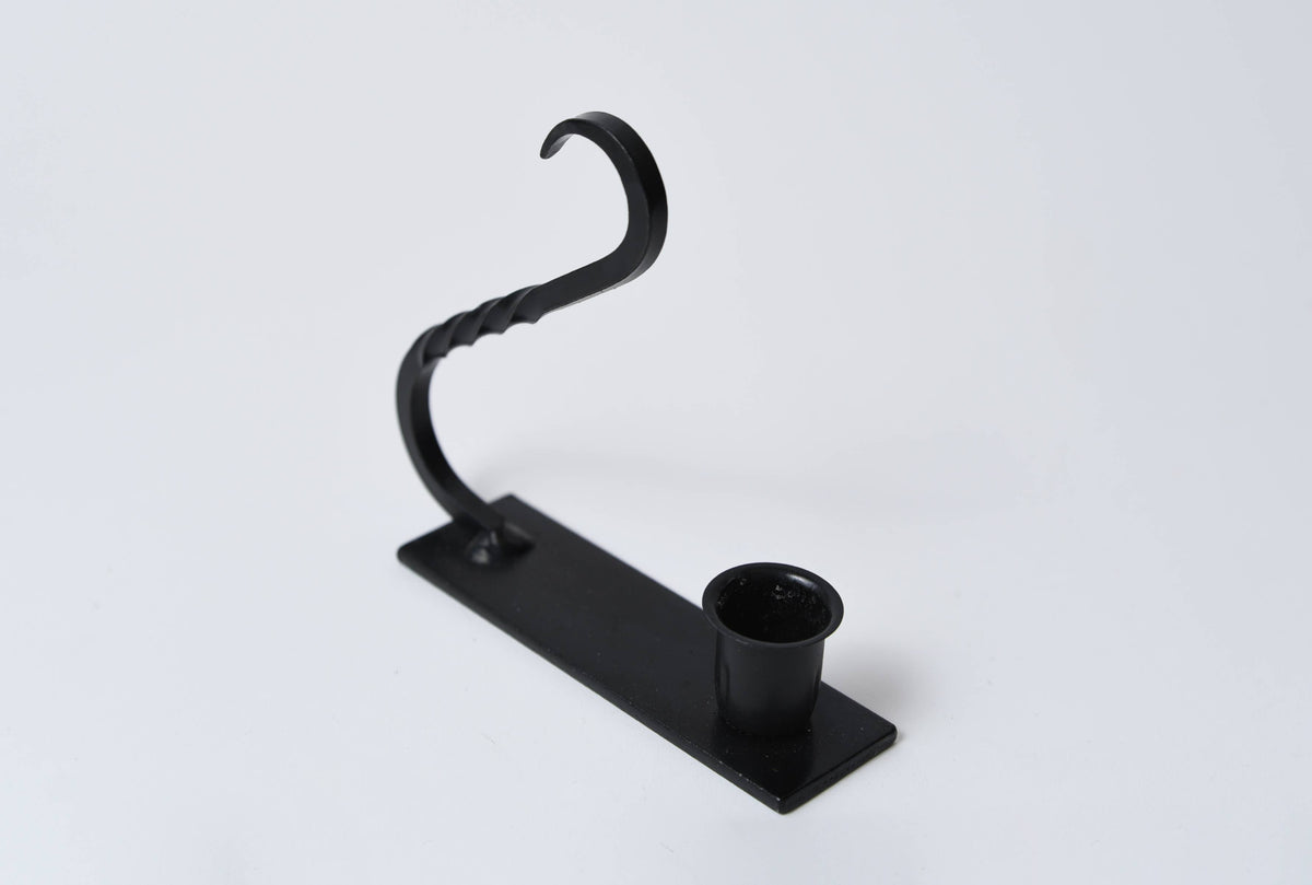 Black iron taper holder with a rectangular base, circular candle cup, and an arched handle with twisted metal detail.