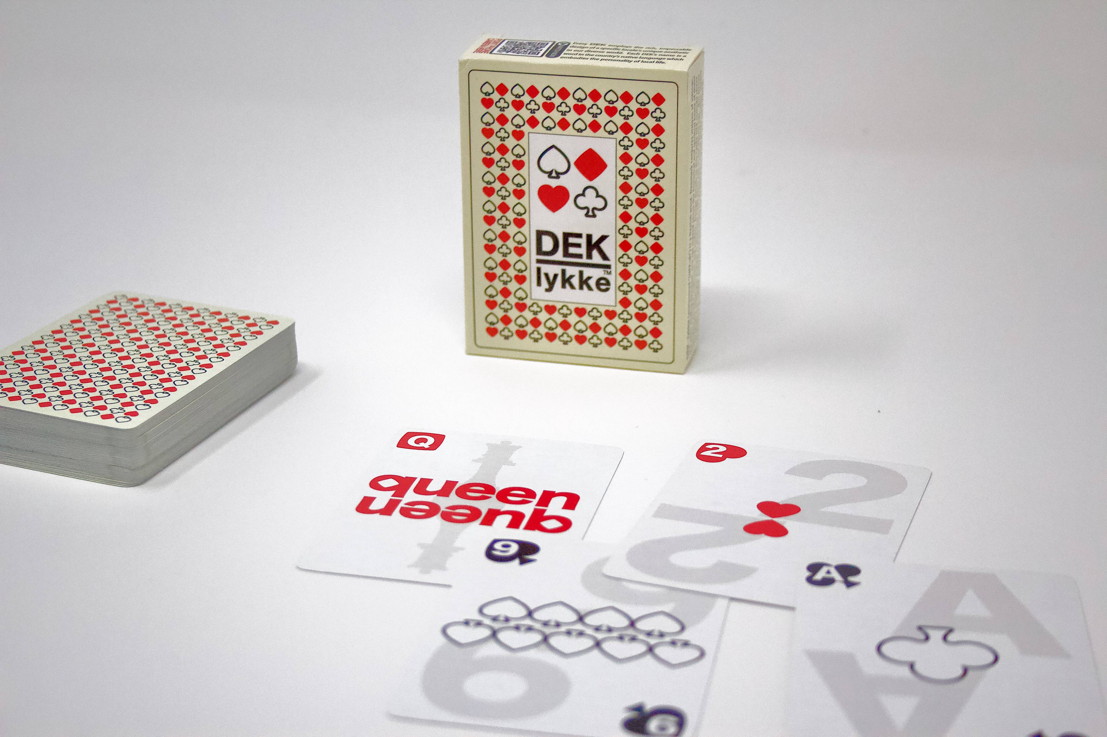 A deck of playing cards called Playing Cards: DEK Lykke (Denmark) is spread out on the table, with some cards face-up, including a queen and a numbered card, exuding joy.