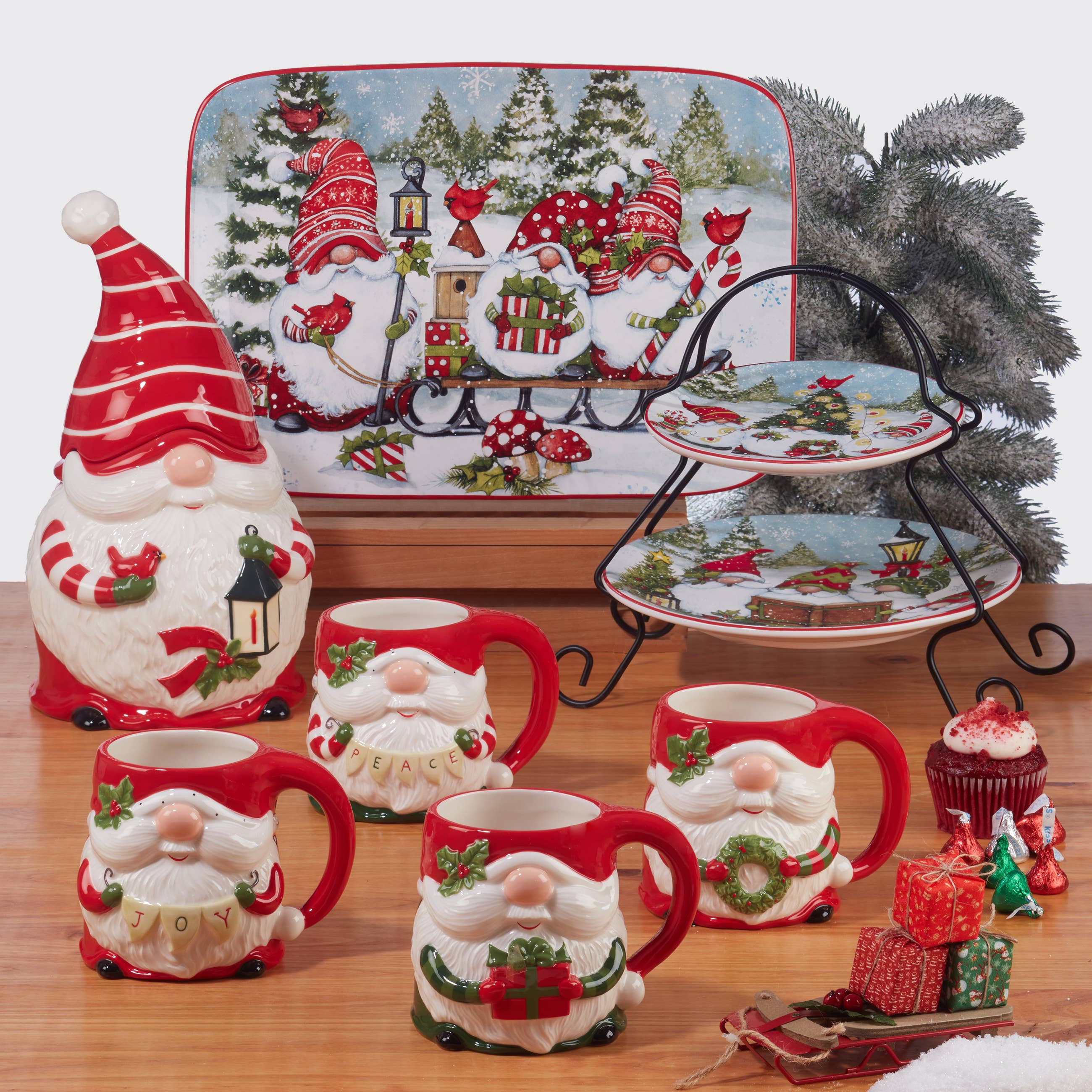 Ceramic Christmas-themed Santa mugs, plates, and a 14x10in Christmas Gnomes Rectangular Platter are displayed on a wooden surface with festive decorations and a faux pine tree in the background.
