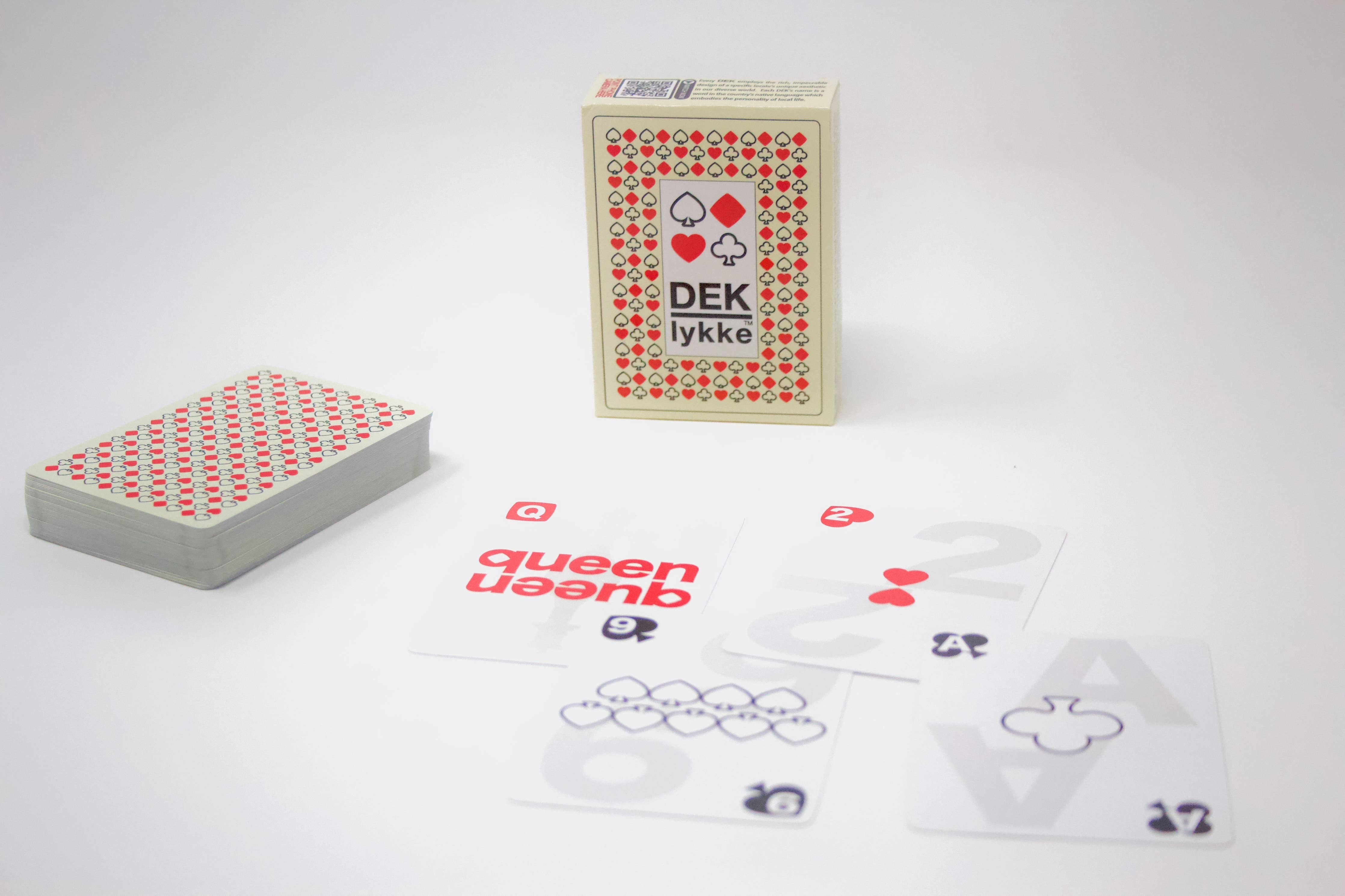 A set of DEK Lykke playing cards from Denmark, featuring some face-up with numbers and suits, radiating joy. The card box and a perfectly stacked deck sit nearby, poised for the upcoming game.