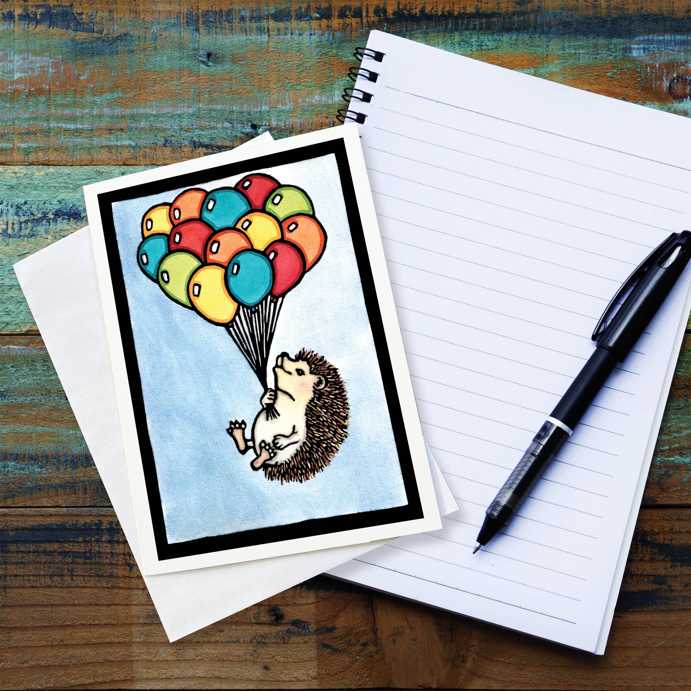 The Up, Up and Away Hedgehog with Balloons 5x7 greeting card features Sarah Angsts art of a hedgehog holding colorful balloons. Blank inside for your personal message and includes an envelope.