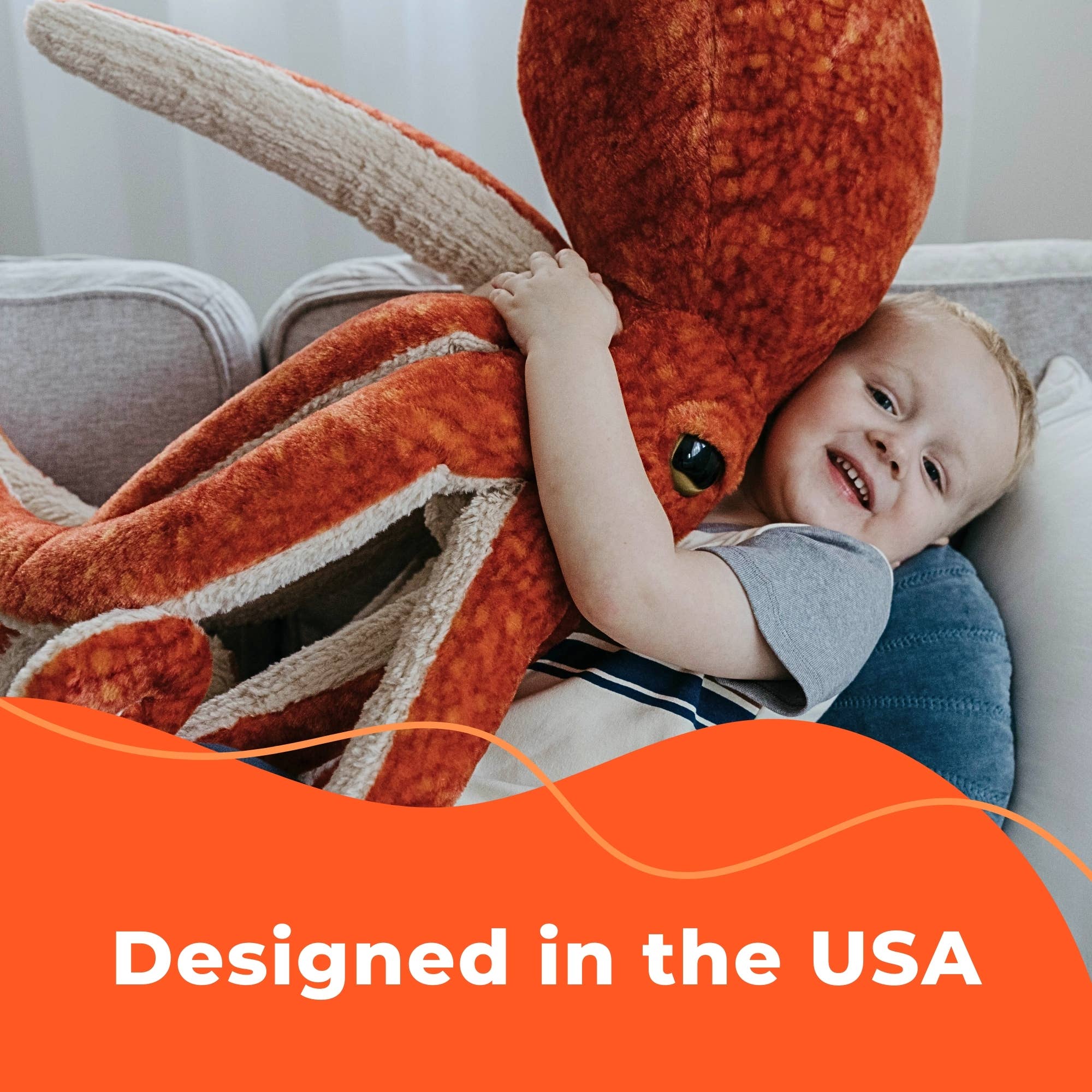 A smiling child hugs a large orange squid plush on the couch, with a Plush: Husky Dog 9 Tall Stuffed Animal sitting nearby. Text overlay reads, “Designed in the USA.”.