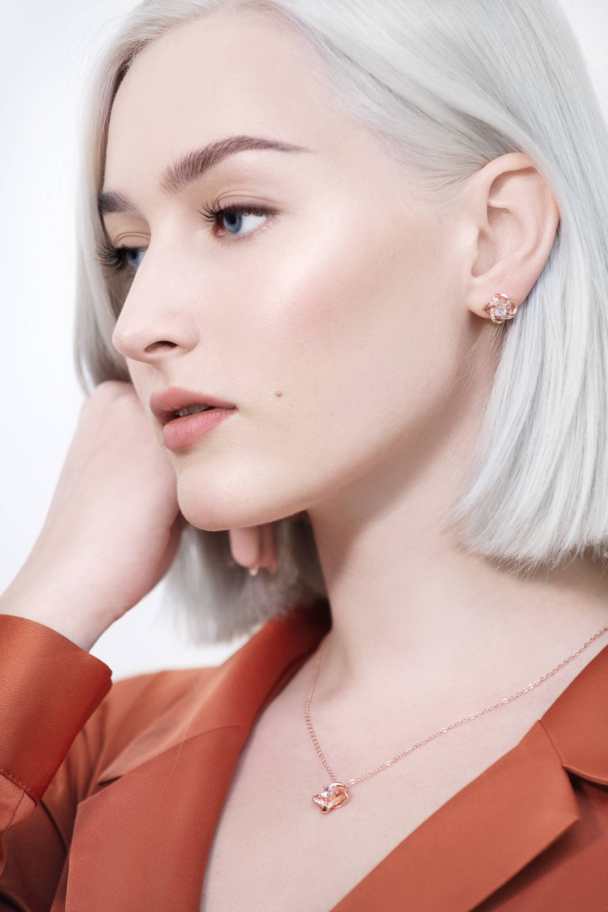 Platinum blonde woman in a rust blazer wears heart-shaped rose gold earrings and the Ice Dance Rose Gold/Sterling Silver Necklace with brilliant cut cubic zirconia on an 18 chain.