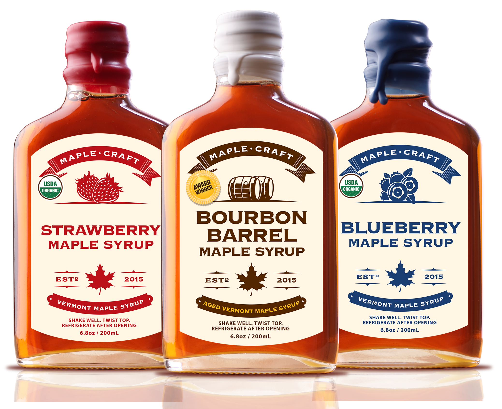 Three bottles of organic, refined sugar-free maple syrup stand side by side with labels: Strawberry - Summer Favorites Maple Syrup (6.8 oz), Bourbon Barrel, and Blueberry. Each features a maple leaf insignia and the year 2015.