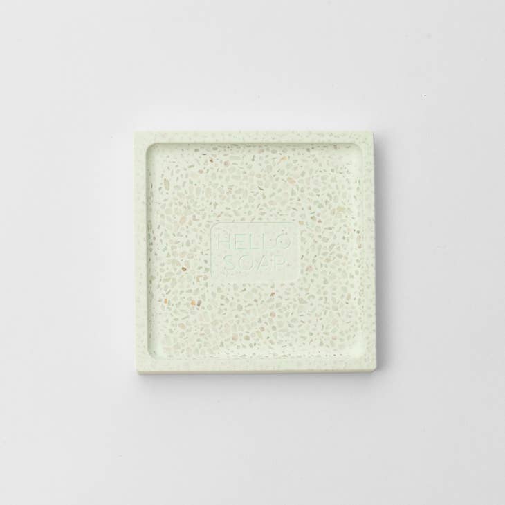 A square speckled soap dish with raised edges and "HELLO SOAP" engraved in the center, crafted from eco-friendly green diatomite, set on a plain white background.