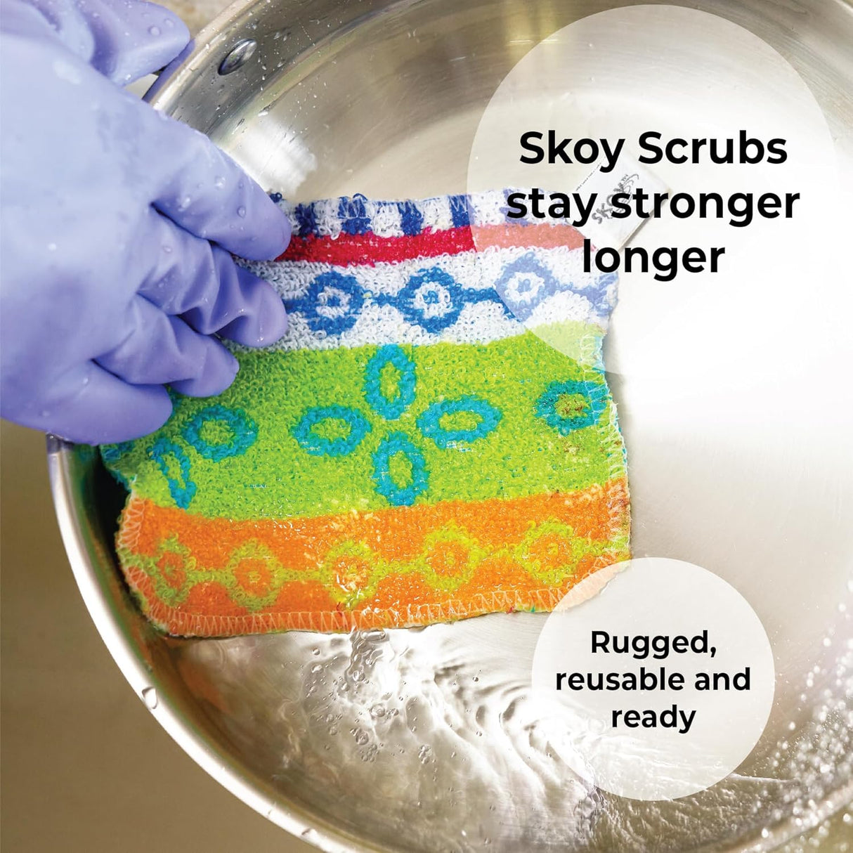 A hand in a purple glove holds Skoy Scrub Cloths Good Clean Fun! by Skoy Enterprises in a metal bowl of water. Text: Strong, reusable, eco-friendly—Skoy scrubbers last longer for good clean fun every time.