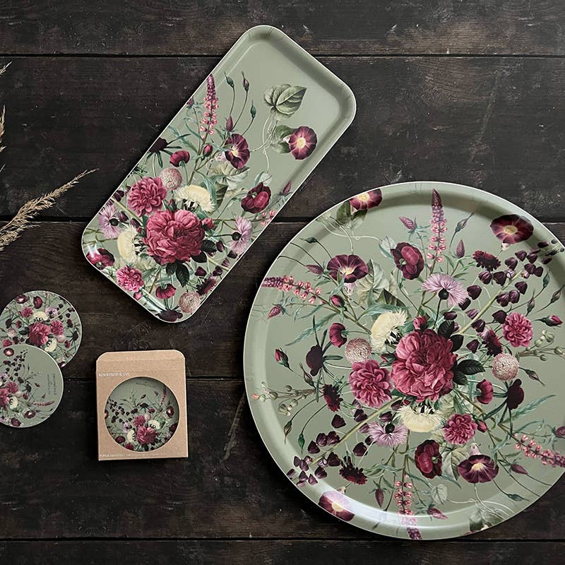 Nordic birch veneer tray and coasters with green, pink, and burgundy floral patterns, arranged on dark wood surface, inside an open cardboard box.