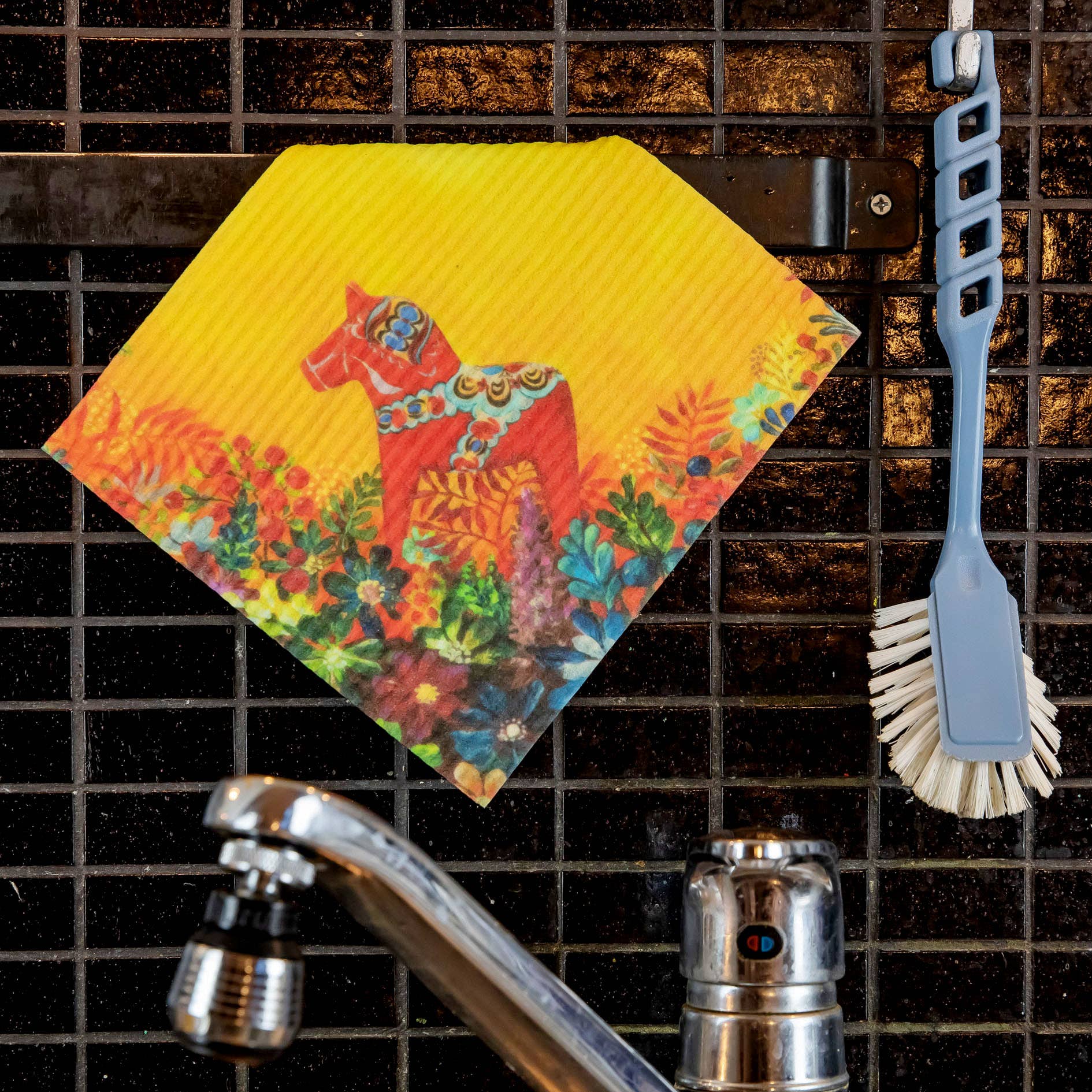 The Light of Grytnäs Dala Horse dish cloth with a red horse and floral design hangs on a rail above the sink next to a dish brush.