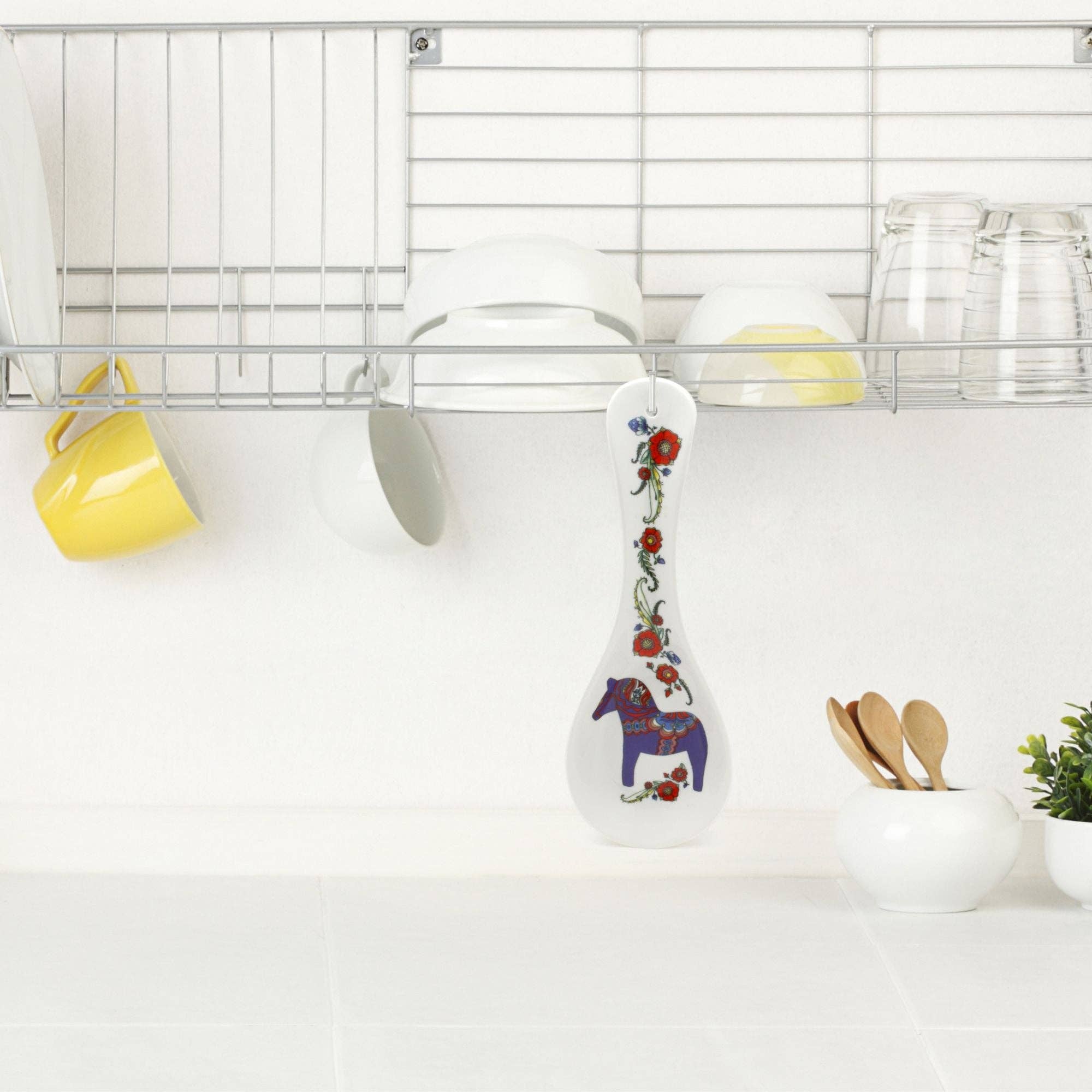 A kitchen features dishes on a metal rack above the counter; in the center hangs the Swedish Blue Dalarna Dala Horse Ceramic Spoon Rest, adding charming Swedish decor.