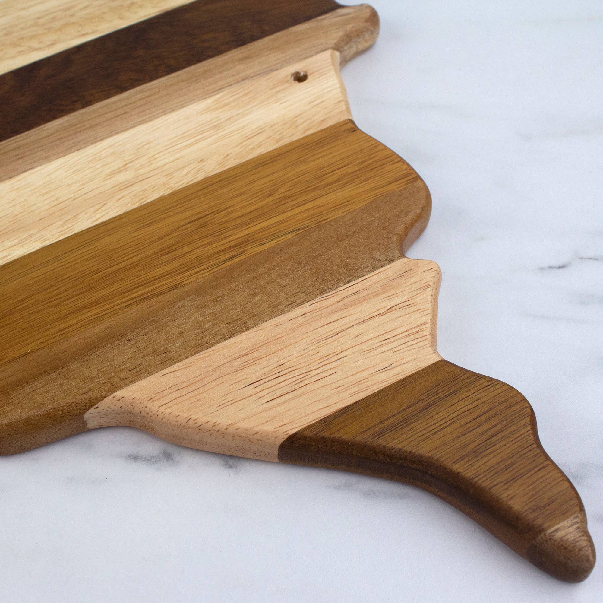 The Minnesota Shiplap Series Serving Board, featuring alternating light and dark wood strips, is shaped like the state of Minnesota and displayed on a white marble surface.