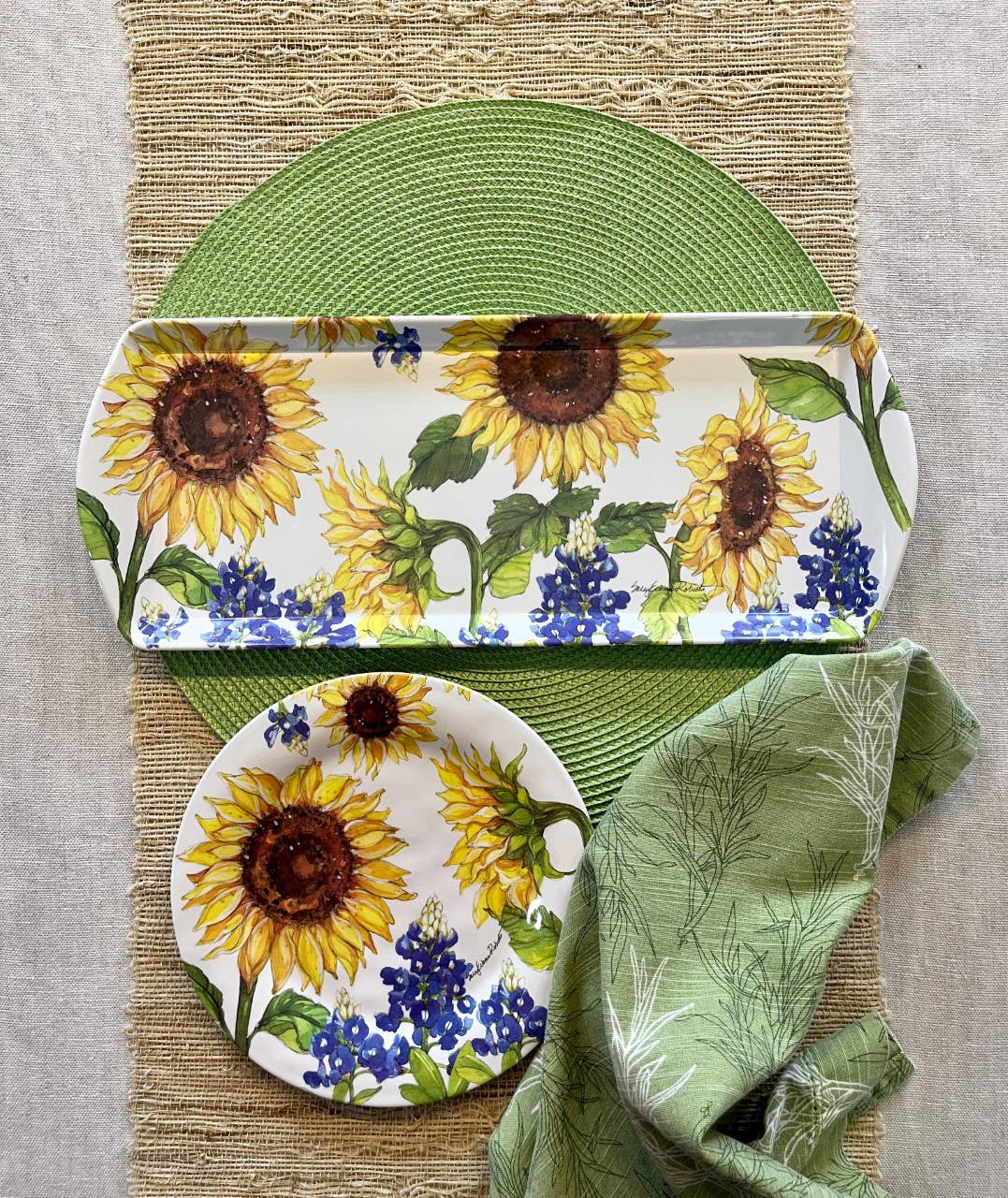The Sunflower & Bluebonnets Floral Loaf Serving Charcuterie Tray is displayed on a green placemat and woven table runner, paired with a folded green napkin for an eco-friendly and stylish tablescape.