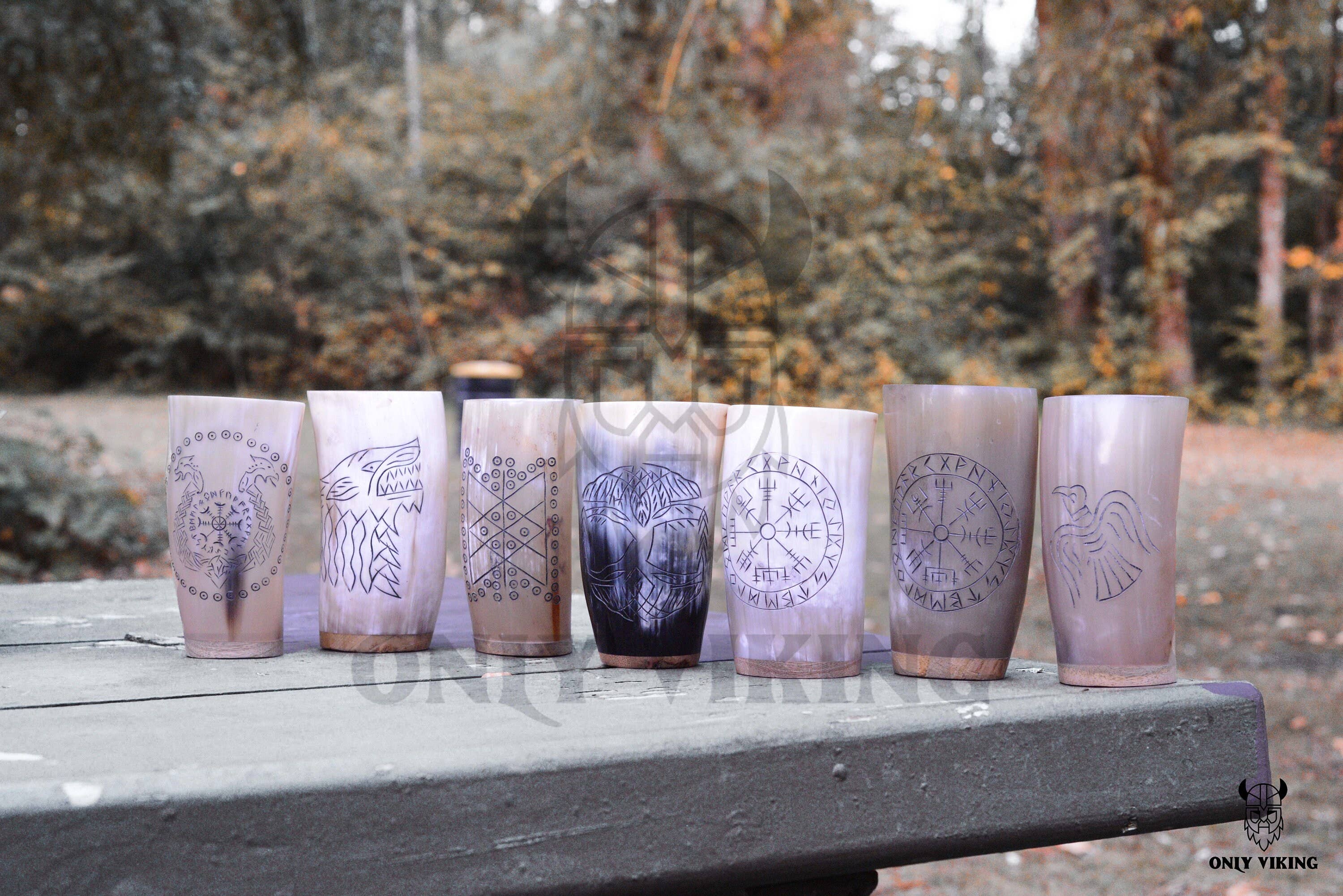 Seven Horn Mug: Beer Stein Drinking Horn Mug Tree of Life 6-9 oz, each featuring Norse symbols, stand upright on a wooden outdoor table amid trees and foliage—blending classic craftsmanship with the rugged beauty of nature.