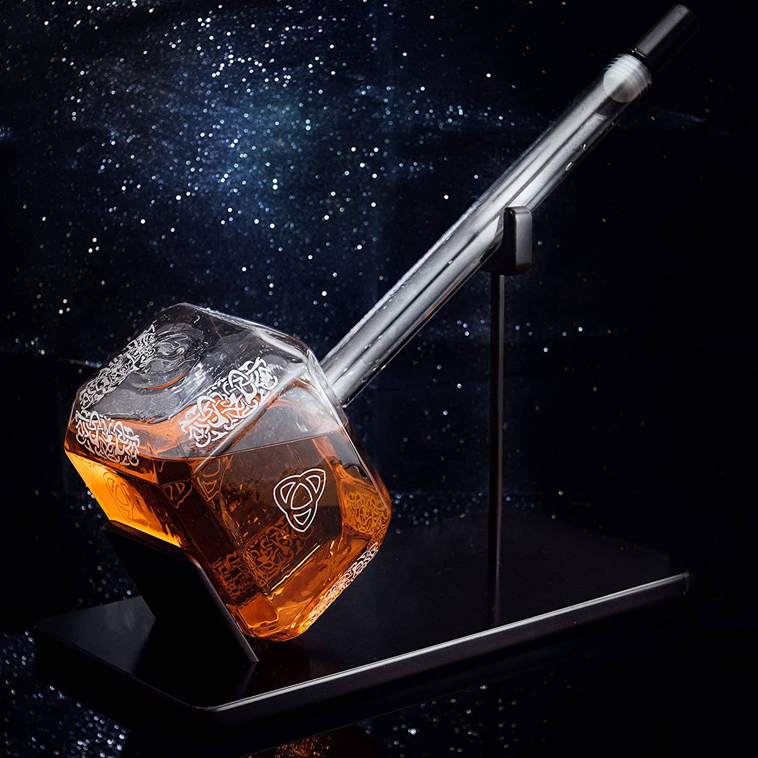 The Decanter: Thor Hammer Whiskey and Wine Decanter 3500ml features a striking Norse-inspired design, filled with amber liquid and displayed on a black stand, set against a captivating starry background.