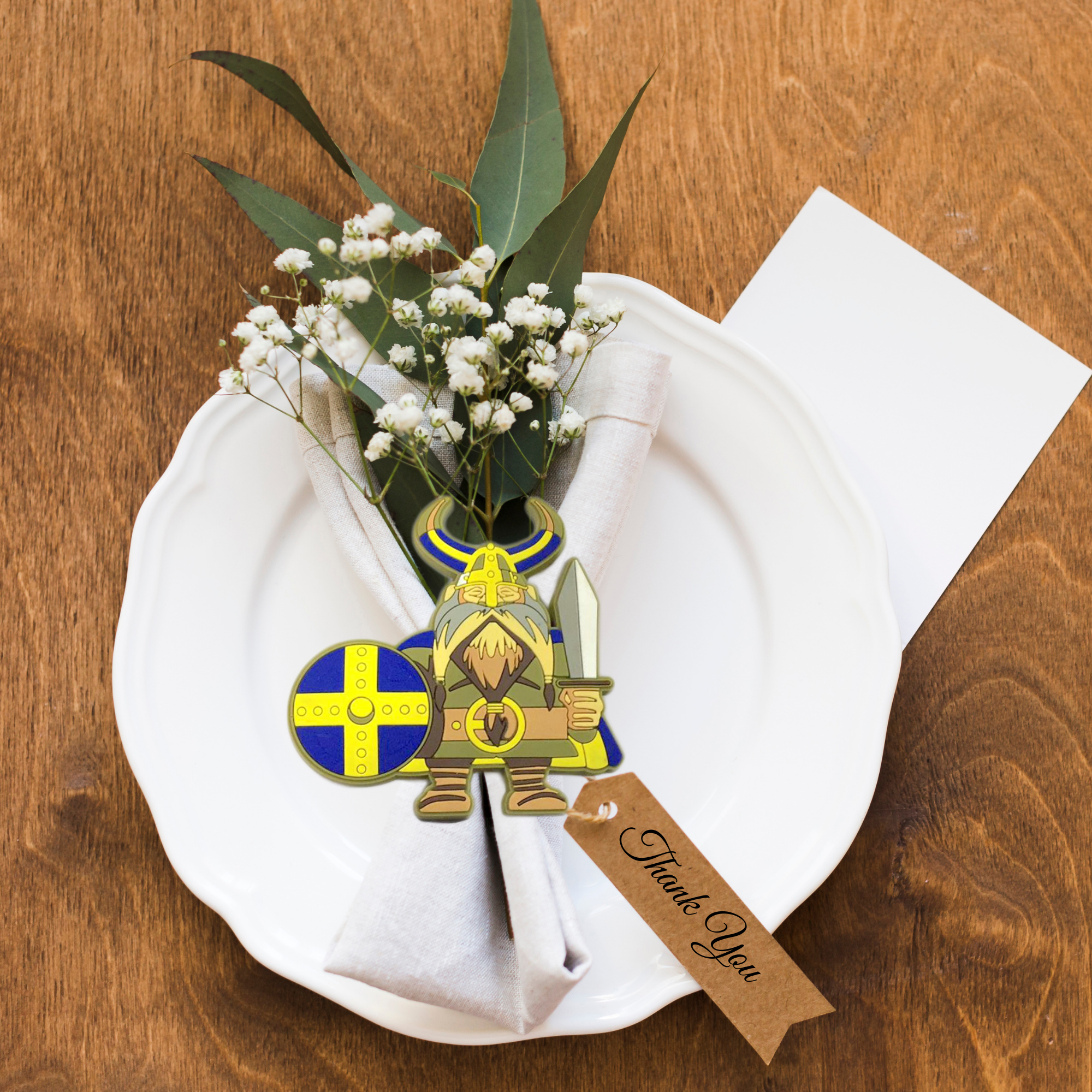 The Magnet: Swedish Viking Scandinavian Kitchen Magnet adds cheerful Scandinavian flair to your setting, featuring a white plate, greenery napkin, cartoon Viking cutout, Thank You tag, and blank card on a wooden table.