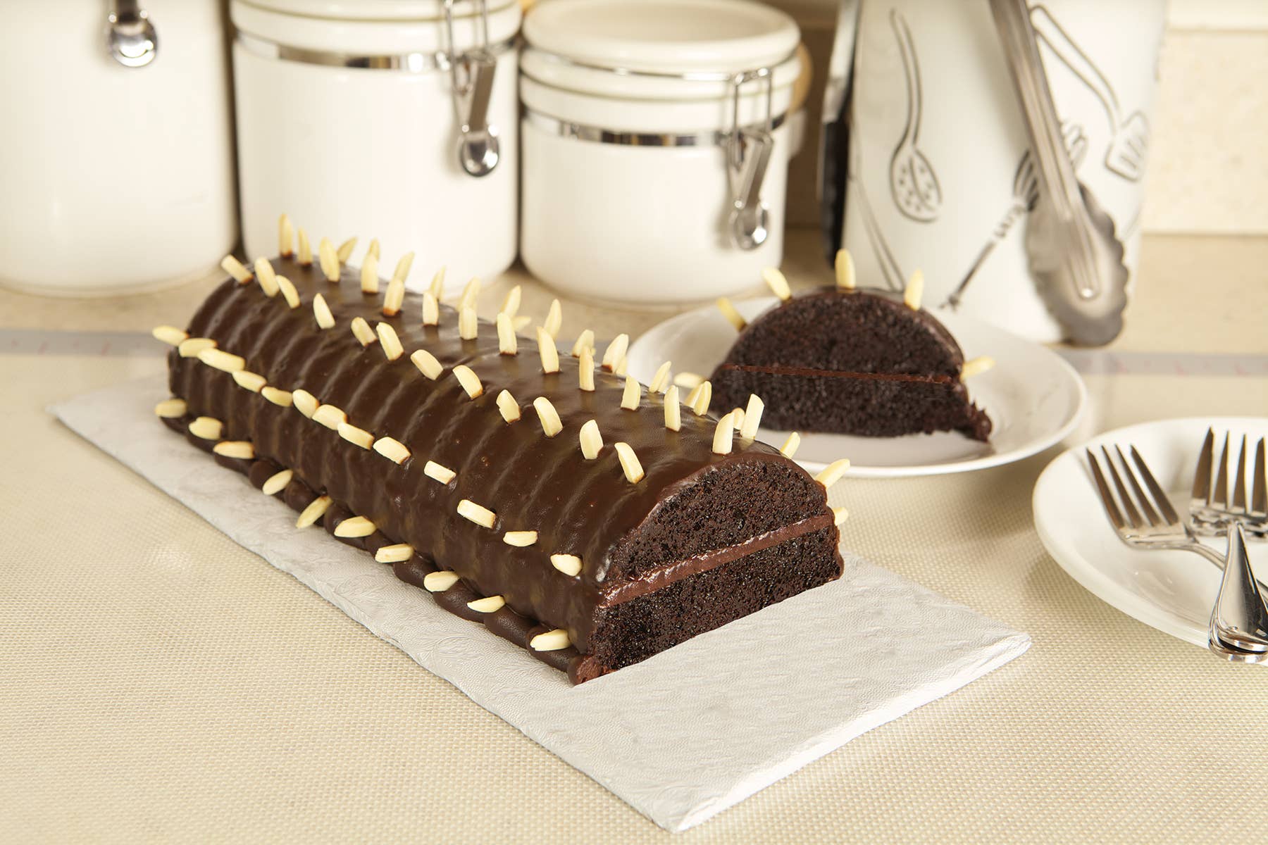 A rectangular almond cake, or Rehrucken, with chocolate glaze and sliced almonds, is displayed on a tray alongside a sliced piece, all baked in the non-stick Rehrucken / Almond Cake Loaf Pan.