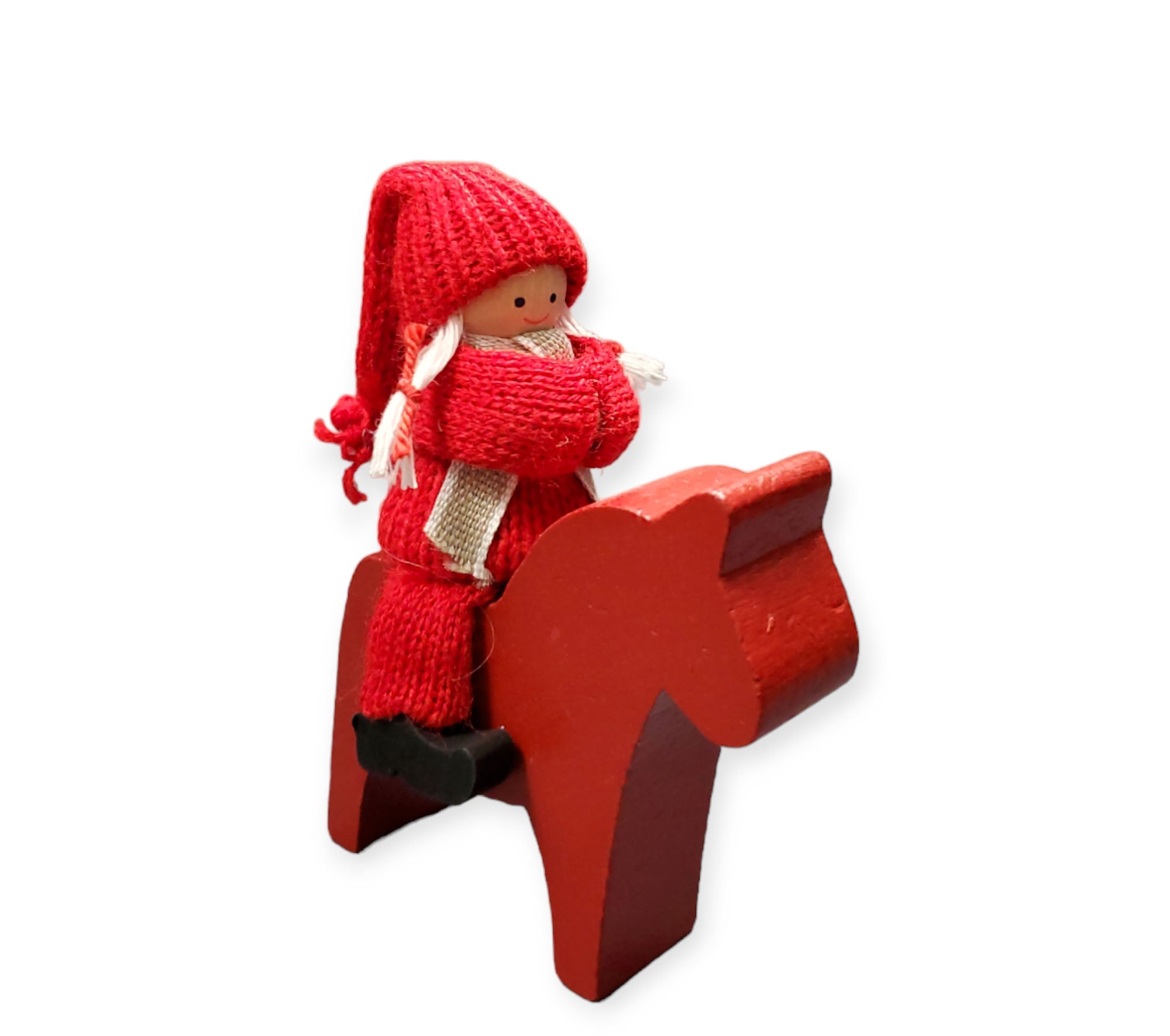 A small figurine in red winter attire rides a handcrafted Swedish Tomte-style Dala horse, according to the product Figurine: Handcrafted Swedish Tomte Boy or Girl on Dala Horse.