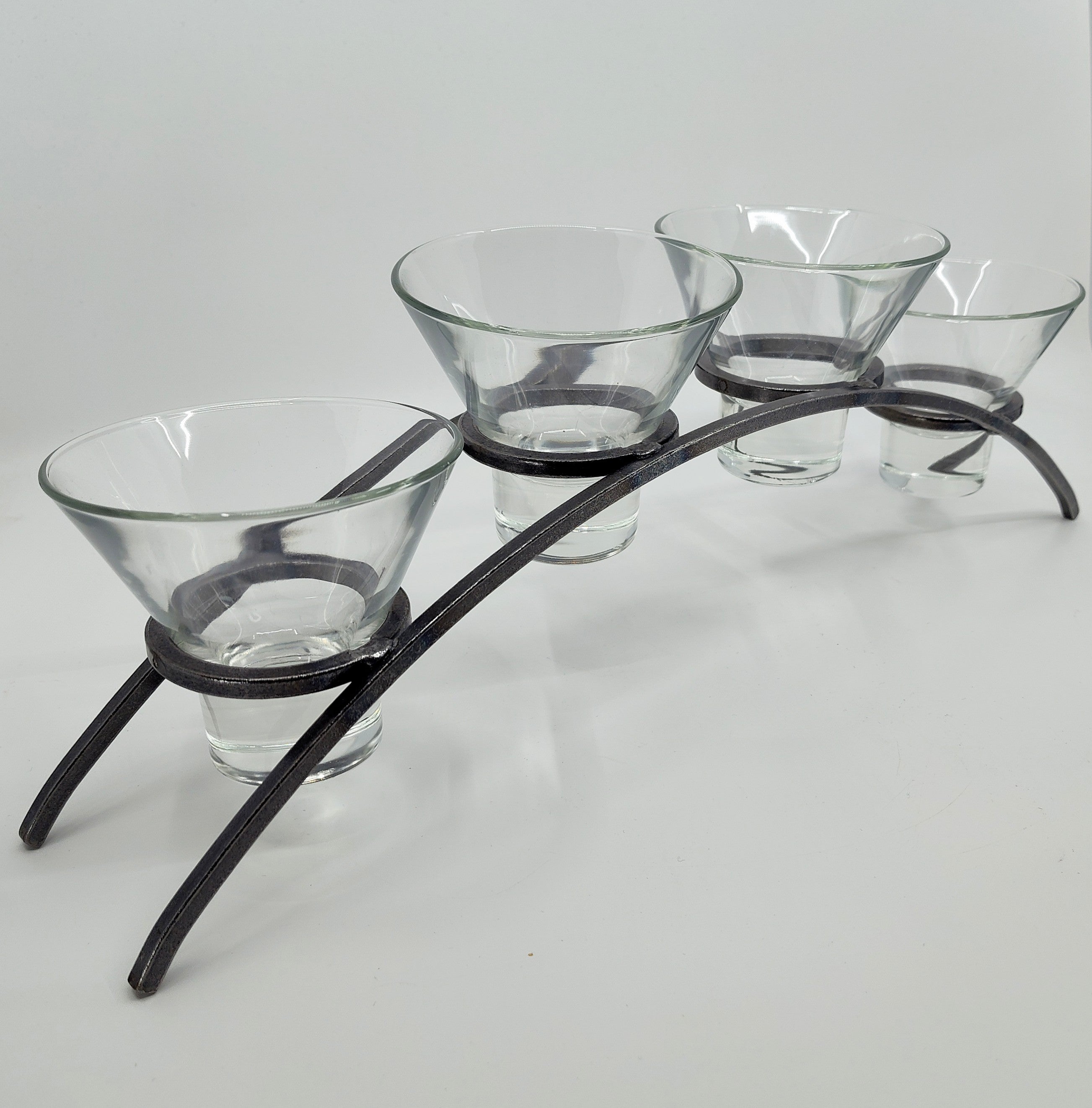 The Danish Iron Arched Candle Holder elegantly supports 4 Leif Cups, perfect for ball candles, on a graceful curved metal stand with two sturdy legs.