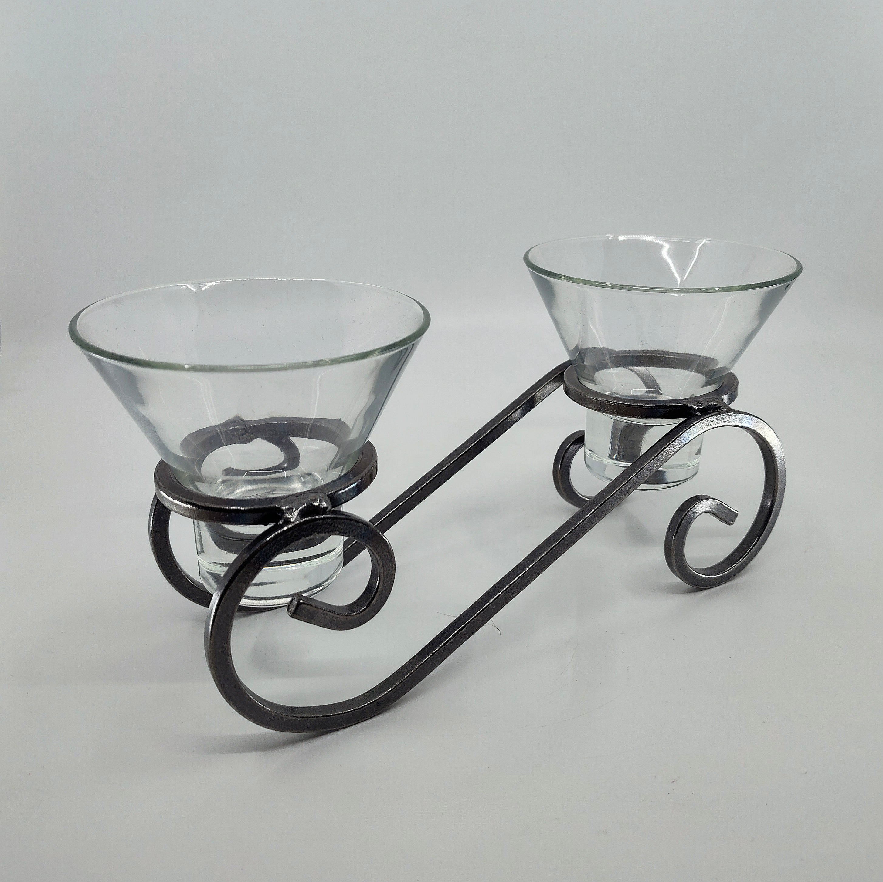 The Danish Iron Candleholder with two Leif glass cups elegantly rests on a decorative metal stand, showcasing an exquisite scrolling design.