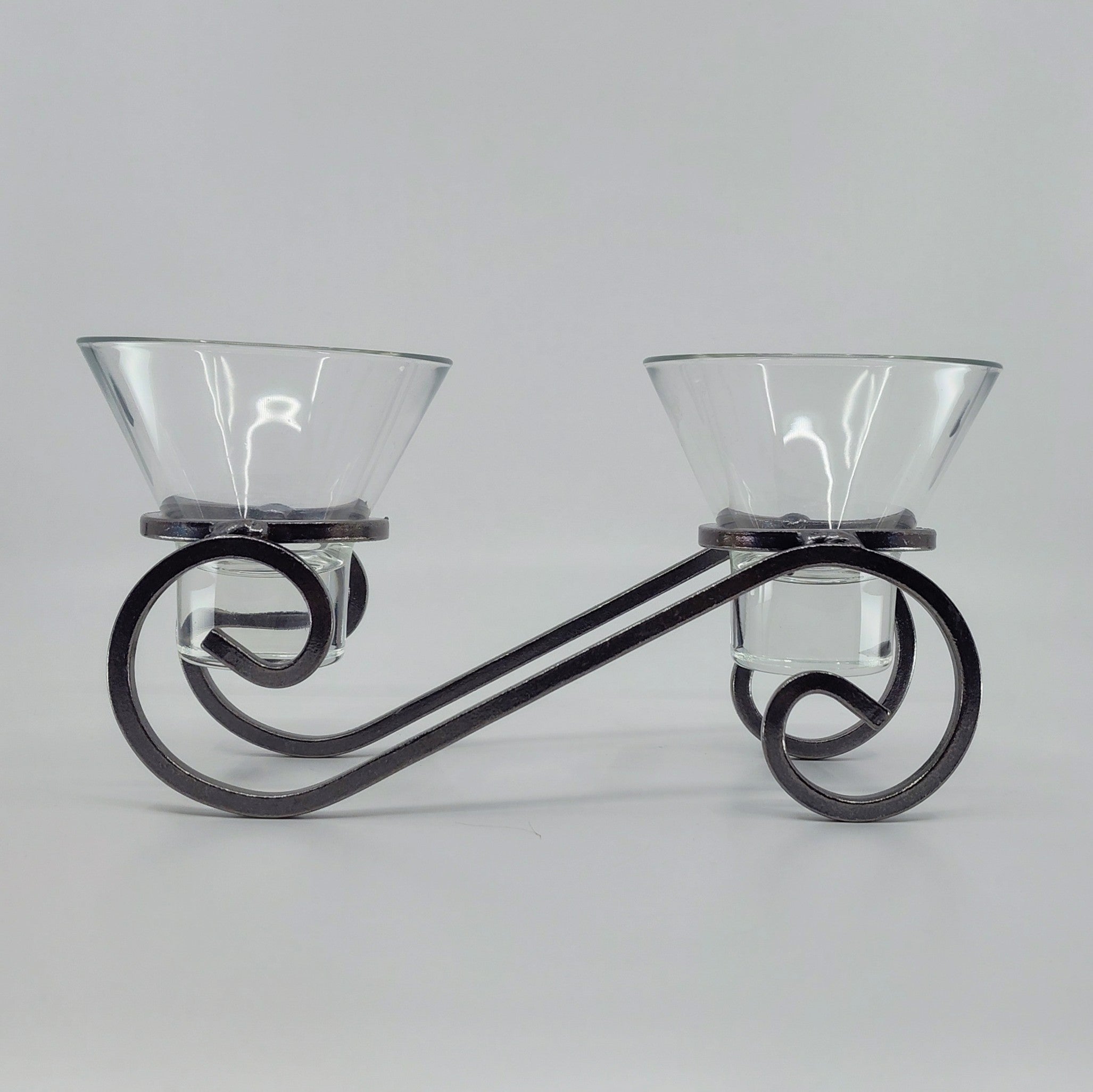 The Danish Iron Candleholder features two Leif glass cups for ball candles, elegantly mounted on a decorative black wrought iron stand with an artistic swirl design, set against a plain gray background.