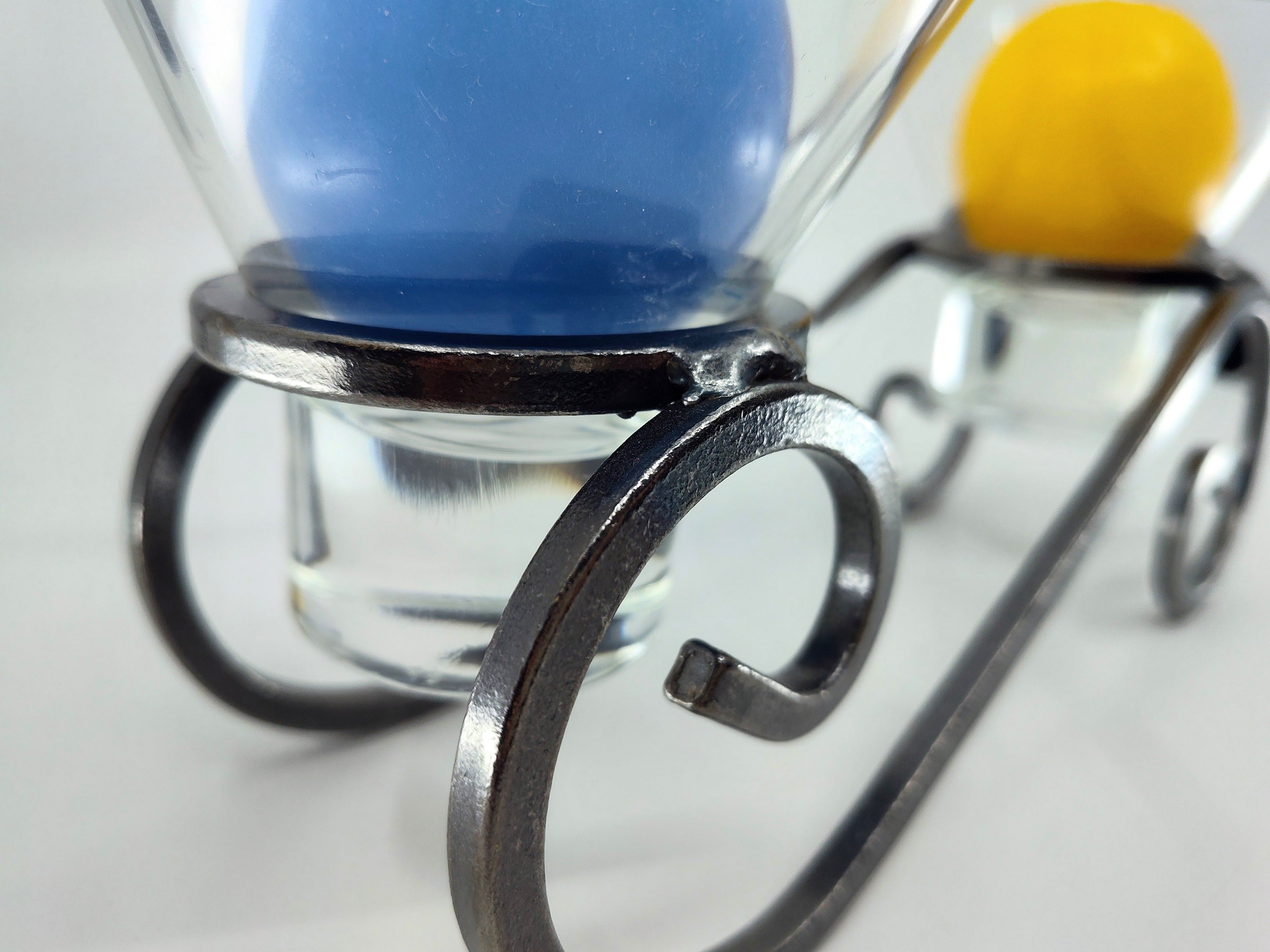 Close-up of two Leif Glass Cups with blue and yellow ball candles, elegantly supported by Danish Iron candleholders on a white surface.