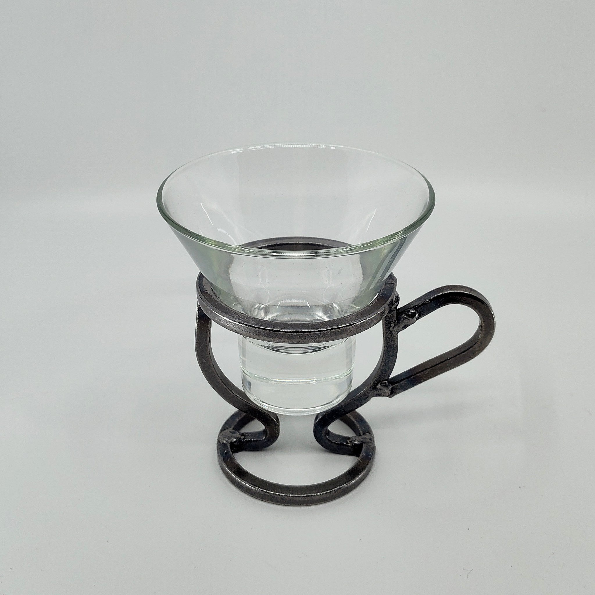 A Danish Iron Coffee Cup holder with a handle elegantly cradles a Leif Glass Cup for Ball Candles against a plain white backdrop.