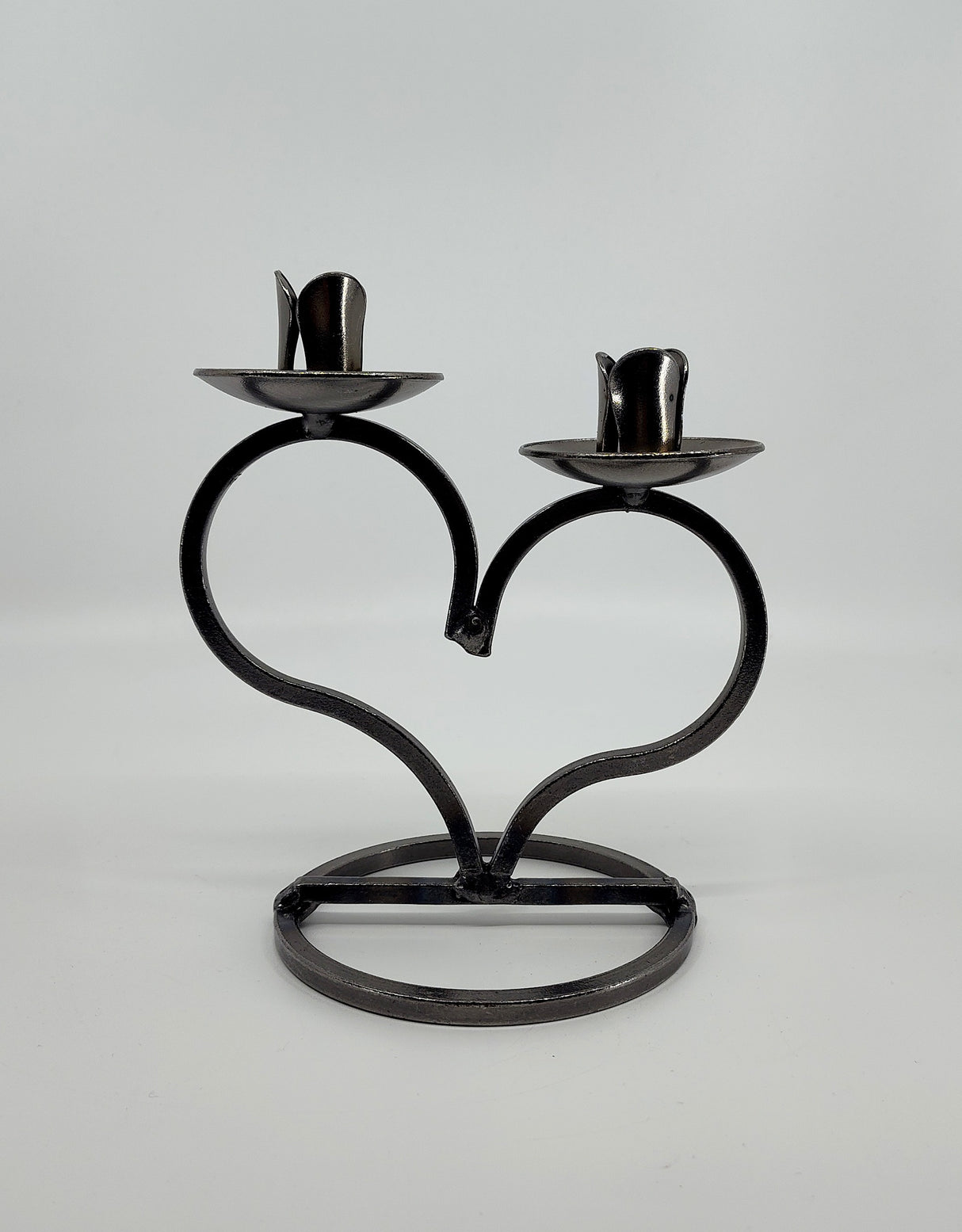 The Candle Holder: Danish Iron Taper Candleholder, featuring a large heart and slots for two taper candles, sits on a sturdy circular base against a plain white background.