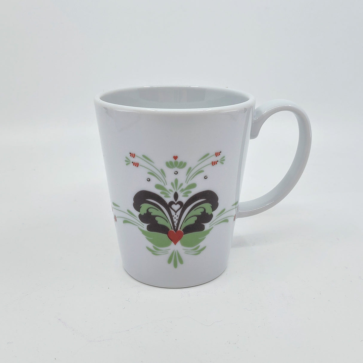 The "Coffee Mug: Anna Viktoria Porcelain Mug with Light Green, Grey, and Red Kurbits" features a handle and a symmetrical Swedish kurbits floral and heart design on the front. The mug is displayed against a plain white background.