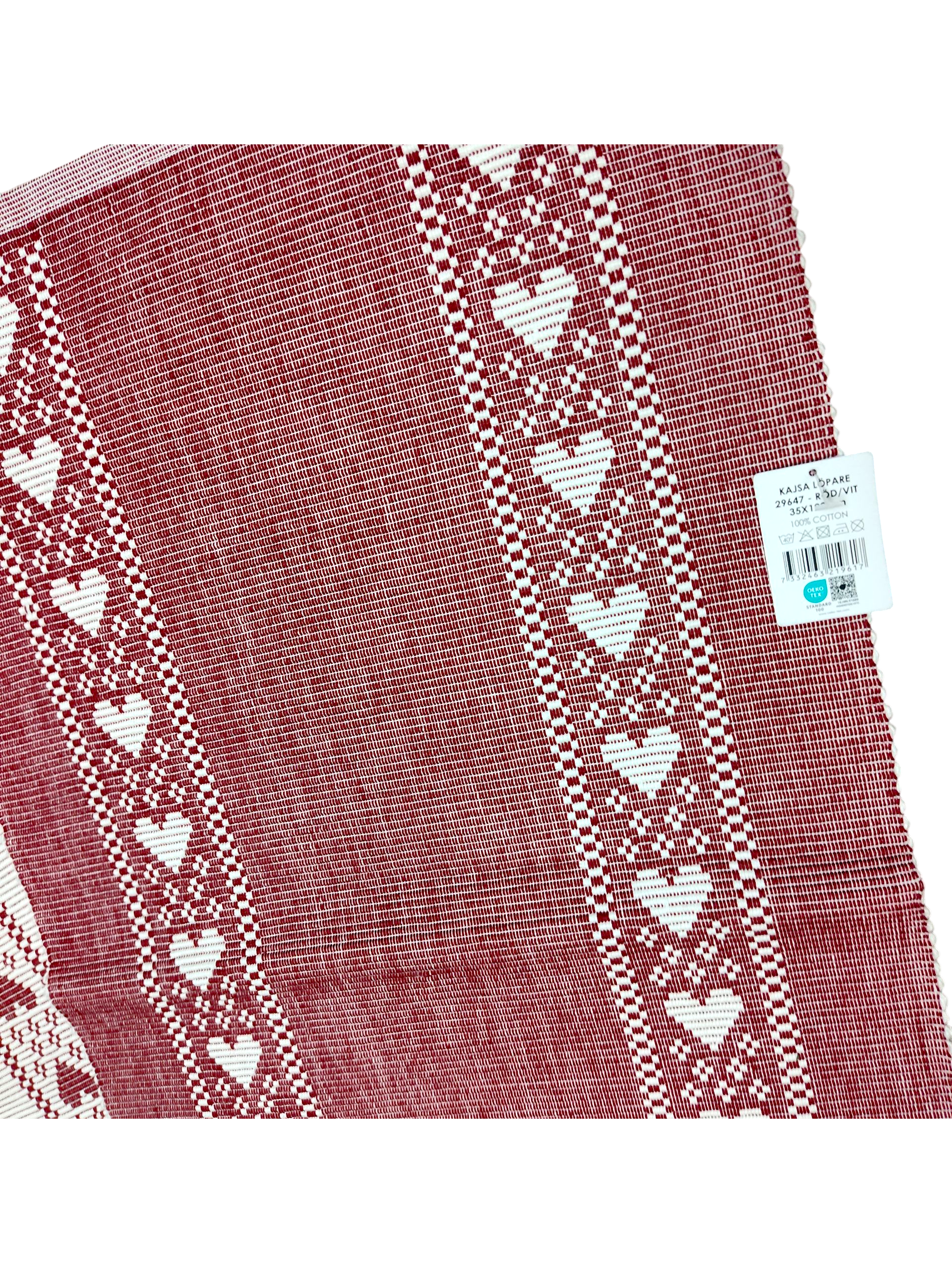 Redlunds of Sweden’s "Kajsa Lopare" table runner is a 14" x 47" red and white woven cotton piece, featuring two rows of white hearts along the edges. A price tag remains attached to the upper right corner.