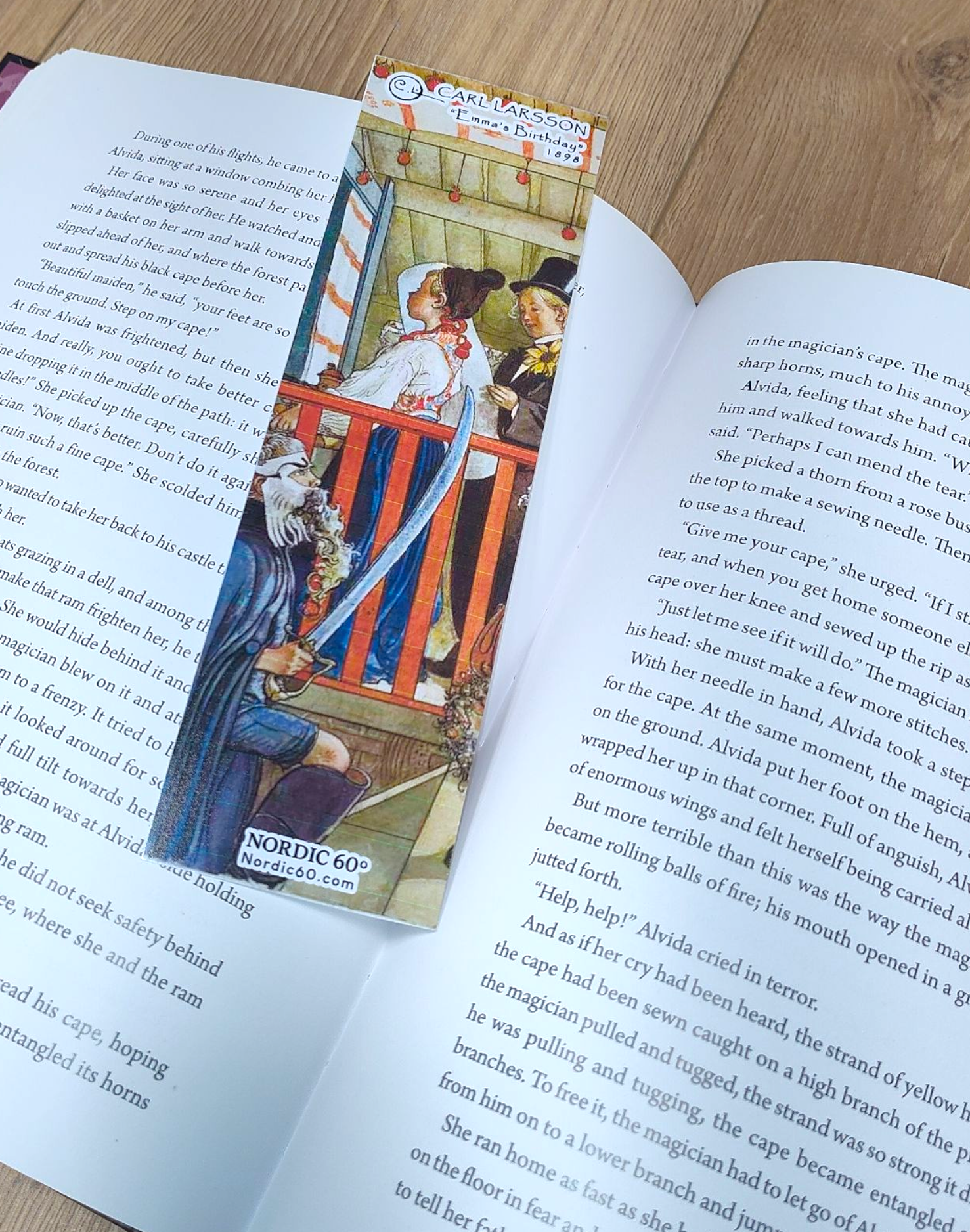 An open book rests on a wooden surface, marked by the “Emma’s Birthday” Carl Larsson bookmark (8.5" × 2.5"), inspired by Swedish art—a charming Scandinavian gift featuring a historical scene.