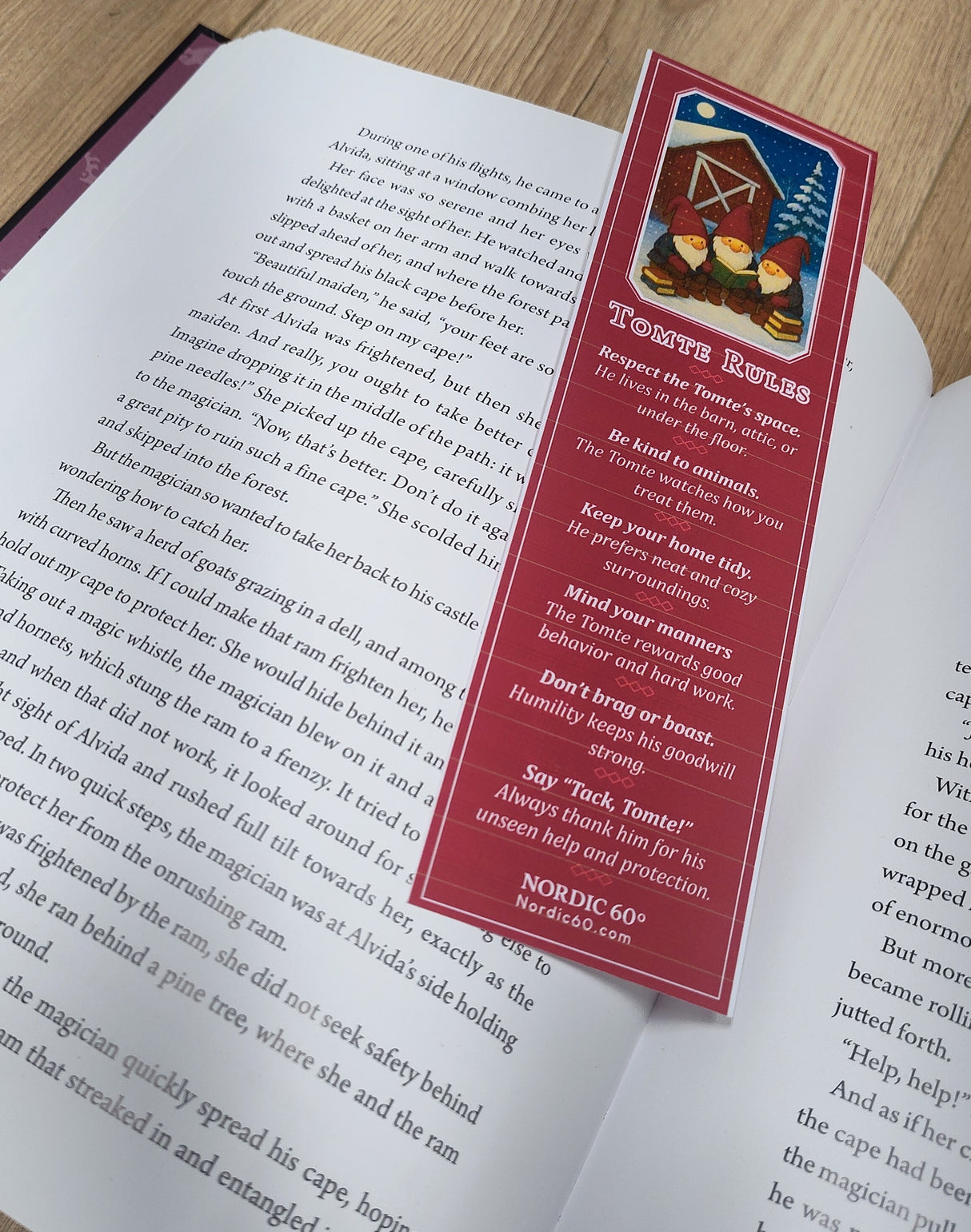 An open book rests on a wooden surface with the “Tomte Rules” bookmark (2.5" × 8.5") placed on its pages, featuring guidelines inspired by Scandinavian folklore.