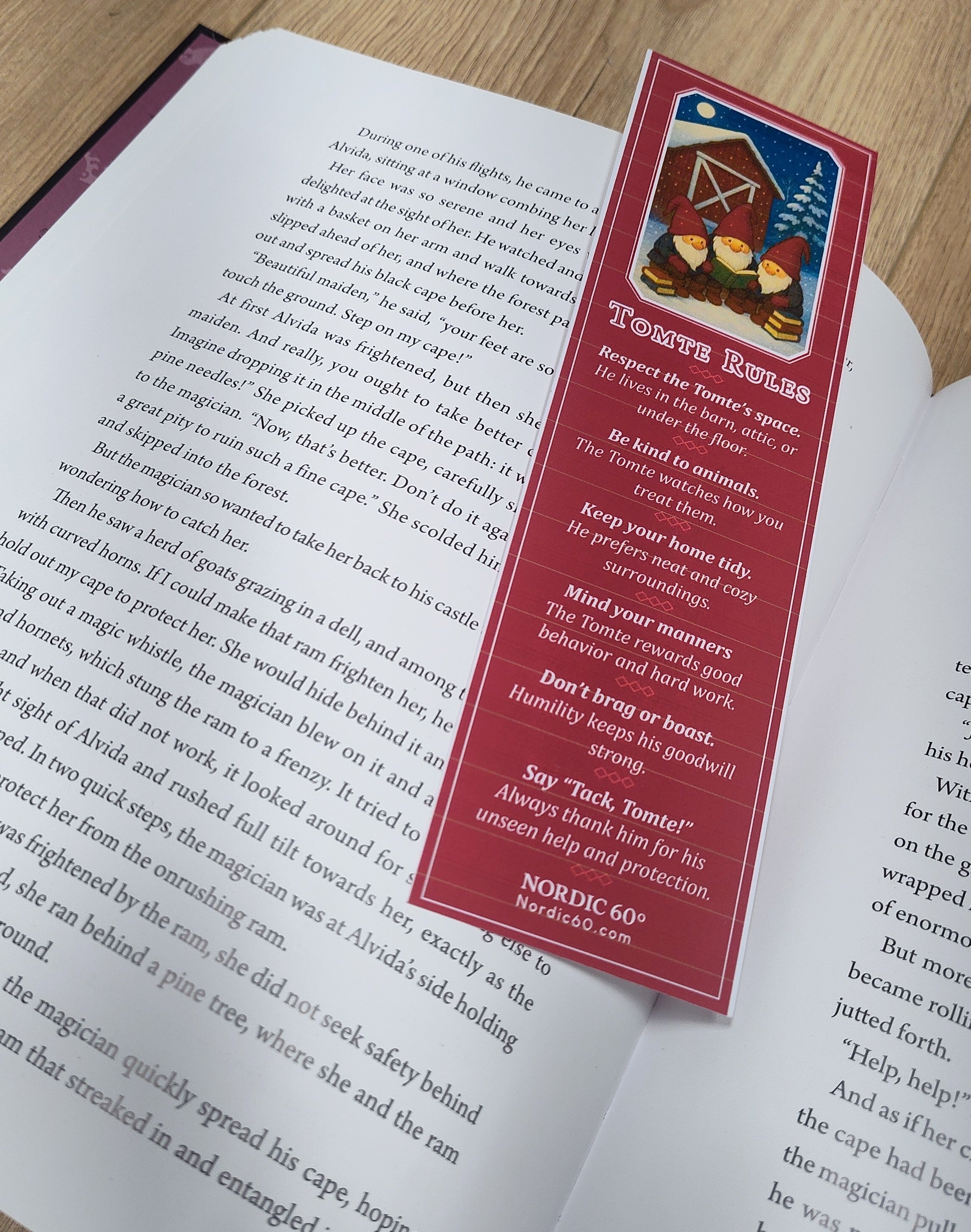 An open book rests on a wooden surface with the “Tomte Rules” bookmark (2.5" × 8.5") placed on its pages, featuring guidelines inspired by Scandinavian folklore.
