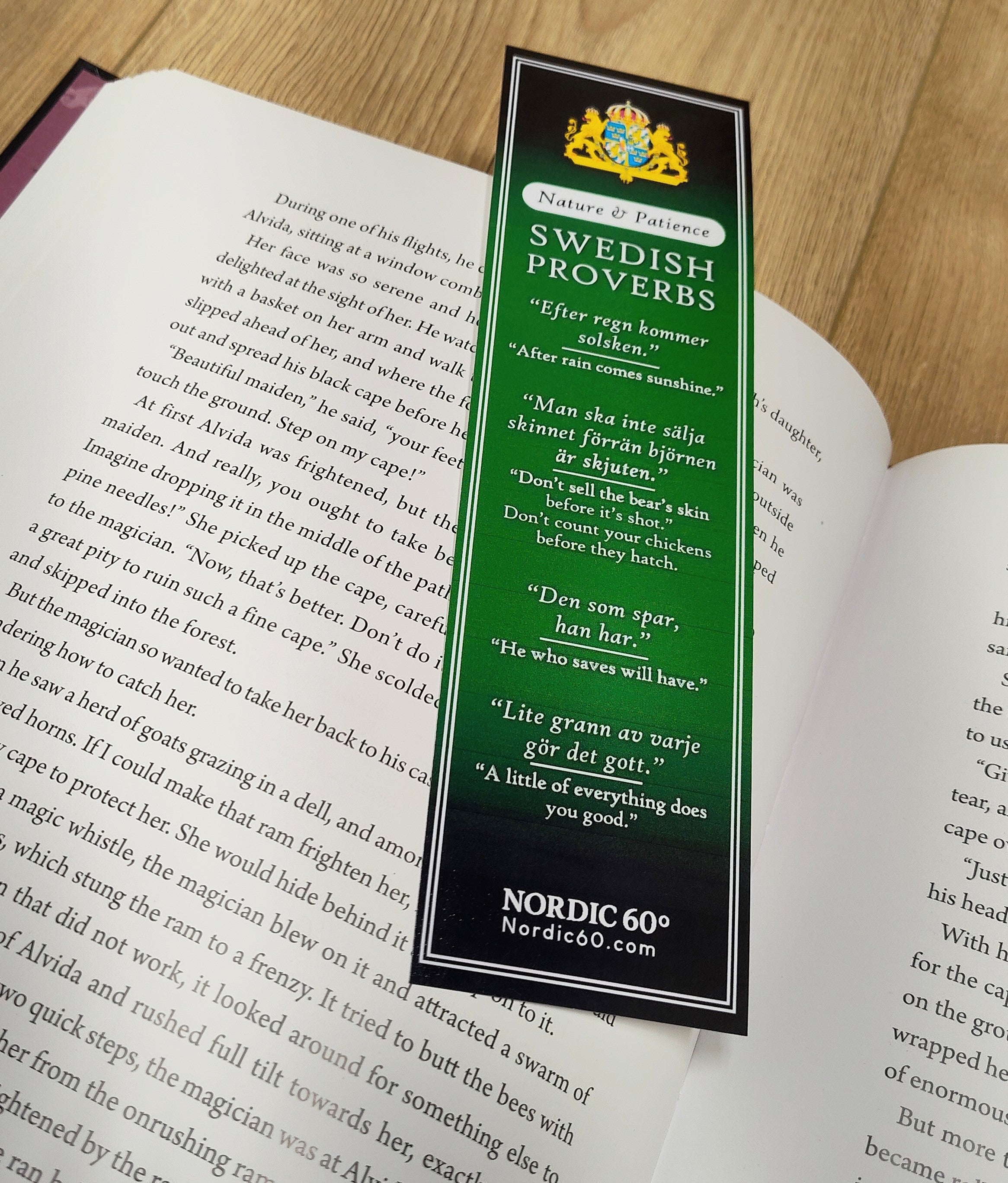 The Bookmark: Swedish Proverbs “Nature & Patience” (2.5" × 8.5") displays Scandinavian wisdom and lies on an open book, set on a wooden surface.