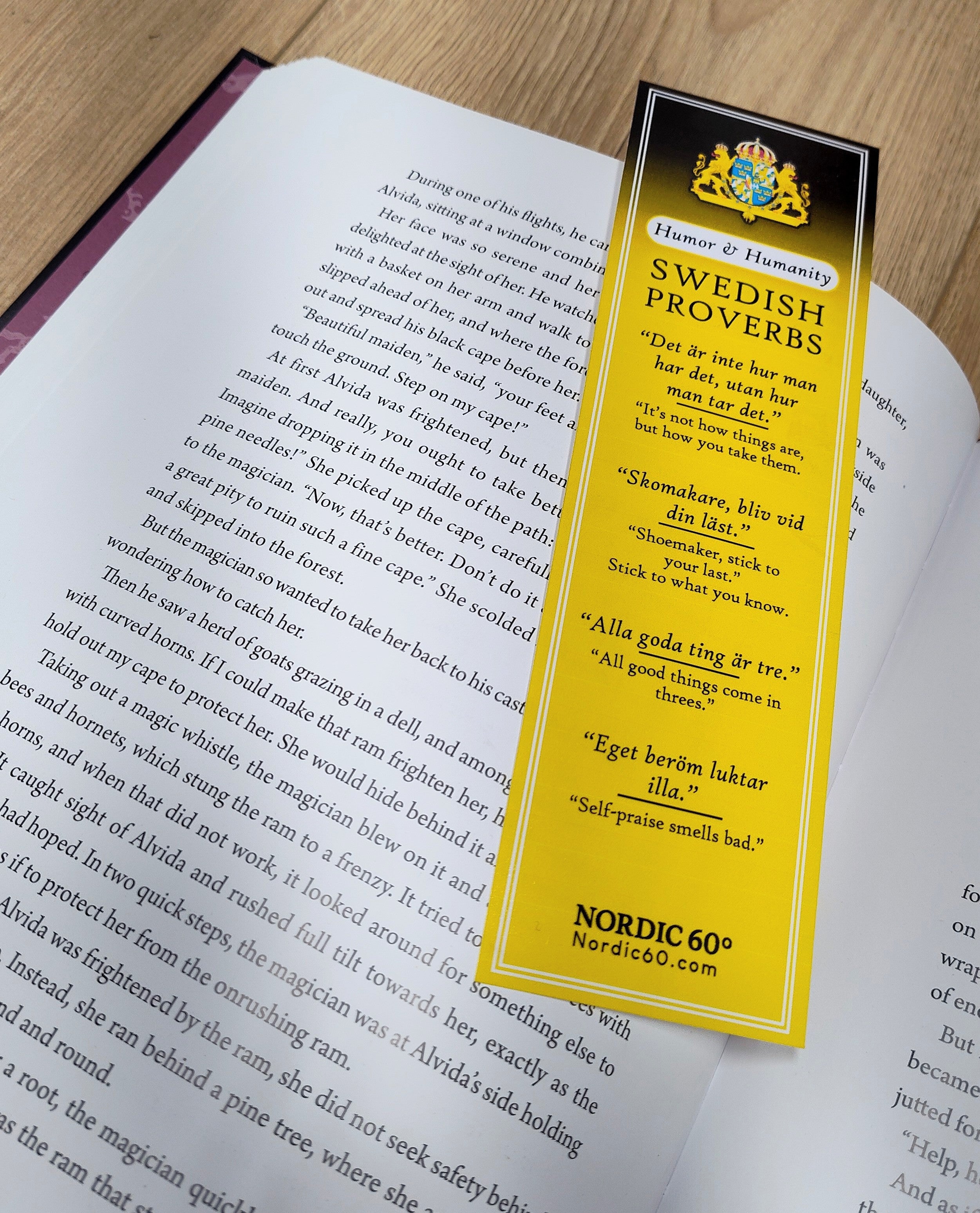 The “Humor & Humanity” Swedish Proverbs Bookmark (2.5" × 8.5")—yellow, Scandinavian design—rests on an open book, displaying bilingual Swedish proverbs celebrating wit and human connection.