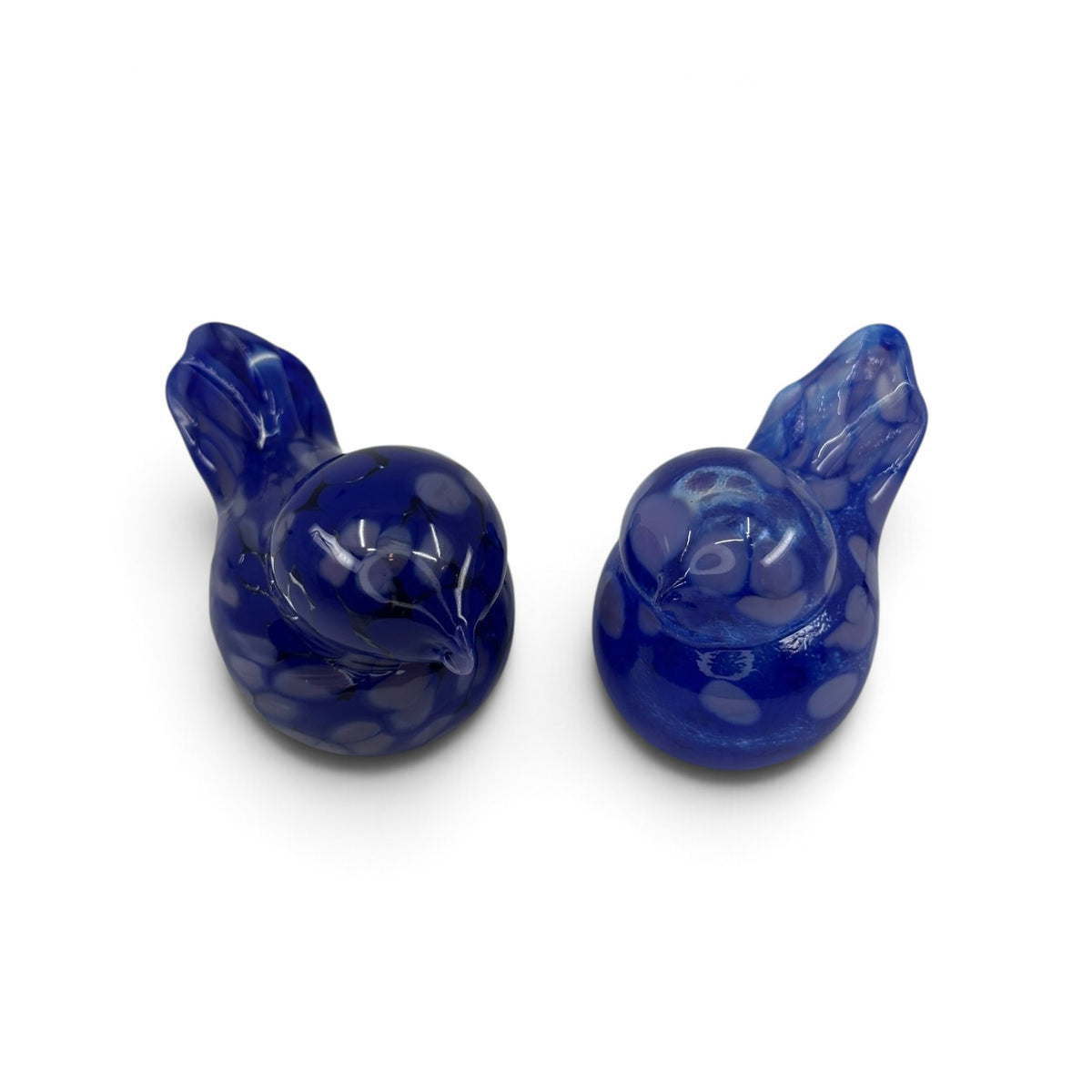 Two blue hand blown glass bird figurines with white spots, viewed from above on a white background. The birds face slightly toward each other.