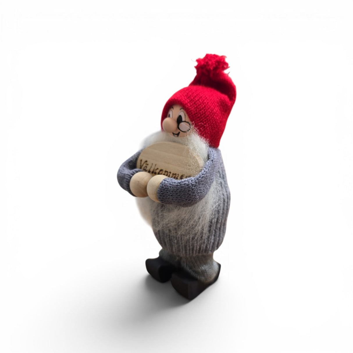 The Swallings Swedish Santa handcrafted figurine stands 6.5" tall with a red cap, gray sweater, glasses, and black shoes, holding a wooden “Valkommen” sign—a charming piece of Nordic holiday décor made in Sweden.