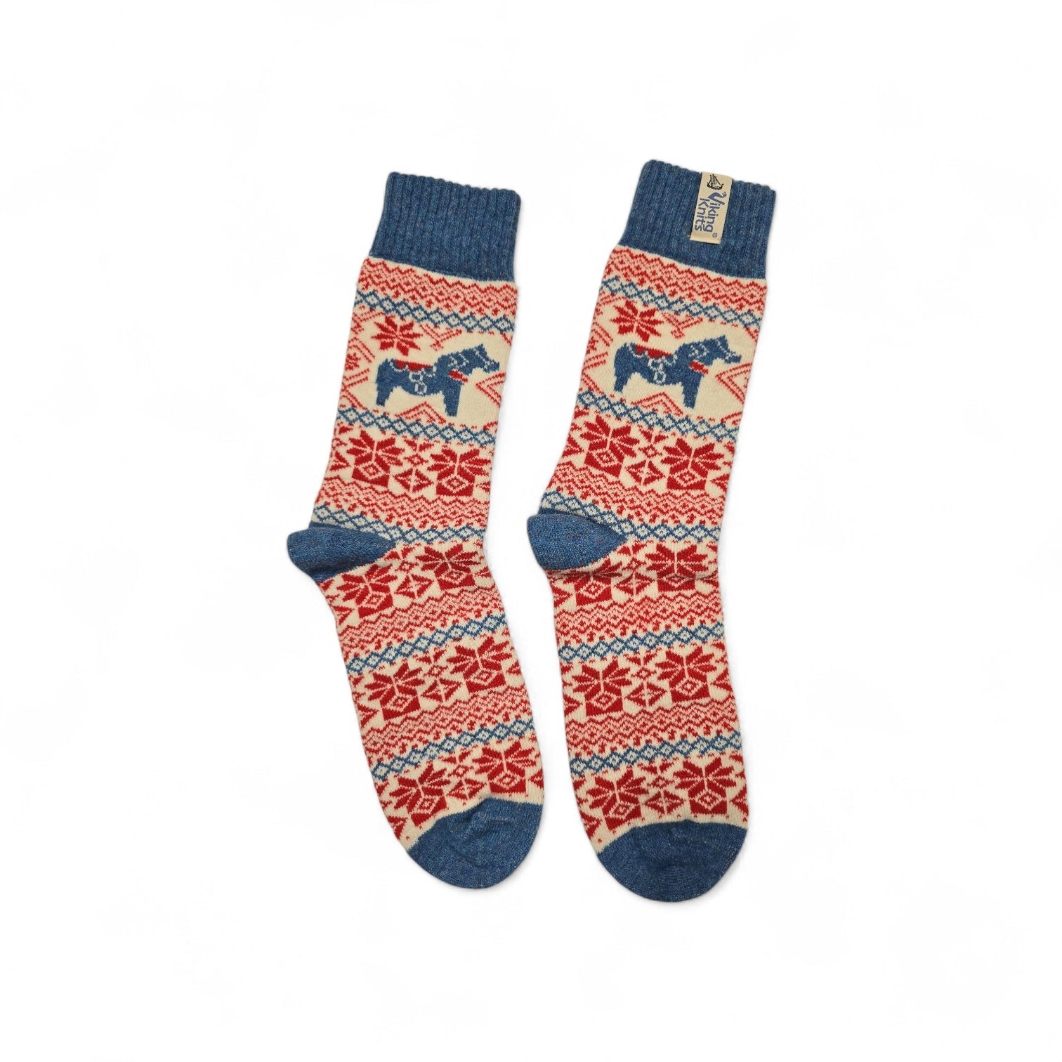 These Viking Knits wool socks feature blue Dala horses and red snowflakes on a beige background with blue toes, heels, and cuffs. Made from 60% wool for warmth and style in a classic Nordic pattern.