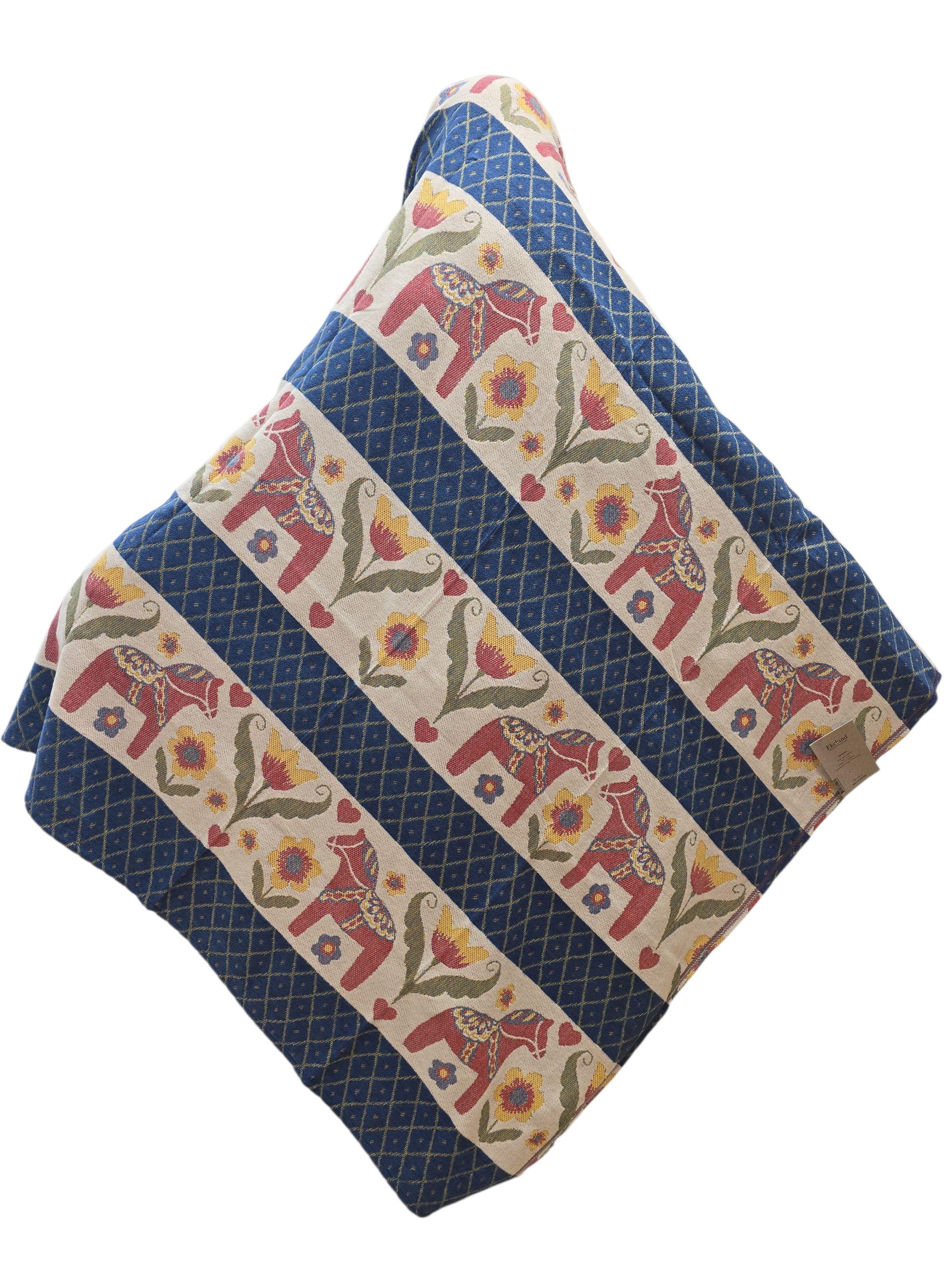 The Dala Horse 100% Cotton Woven Blanket by Ekelund of Sweden (55"x75") features blue diamond patterns with alternating rows of elephants, flowers, and leaves in red, yellow, and green.