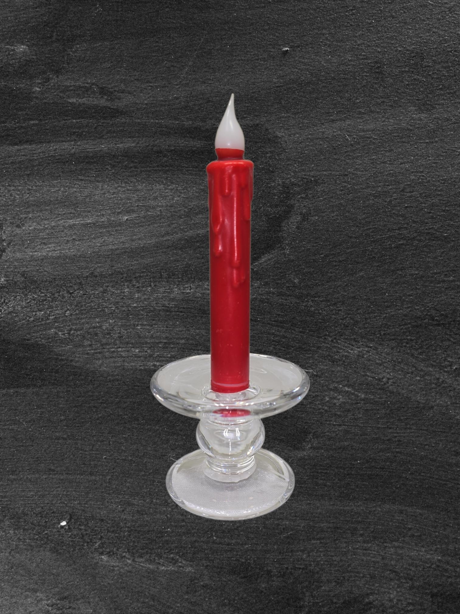 A red wax candle with drips stands in a clear Glass Dual-Size Reversible Candle Holder for taper, ball, or pillar candles, set against a dark textured background.