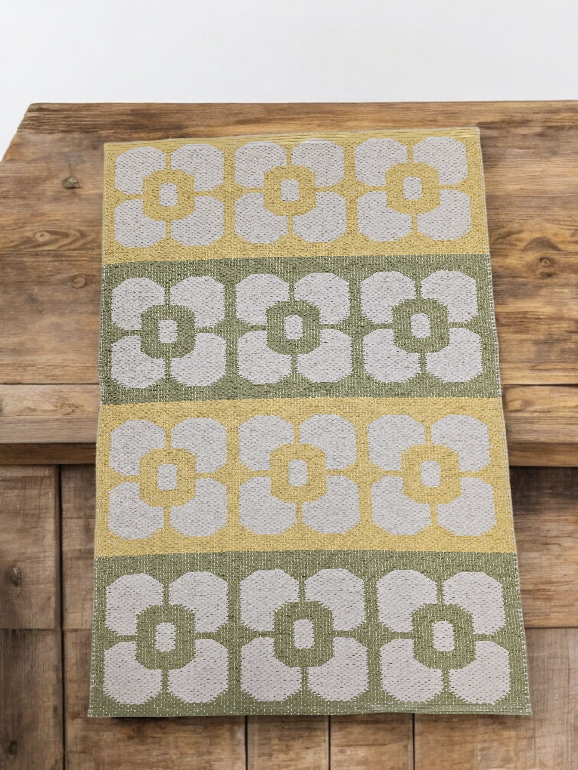 The Horredsmattan Florian Vinyl Rug features rows of stylized white flowers in yellow, green, and gray. Durable and eco-friendly, this modern rectangular rug looks stunning on wooden surfaces.