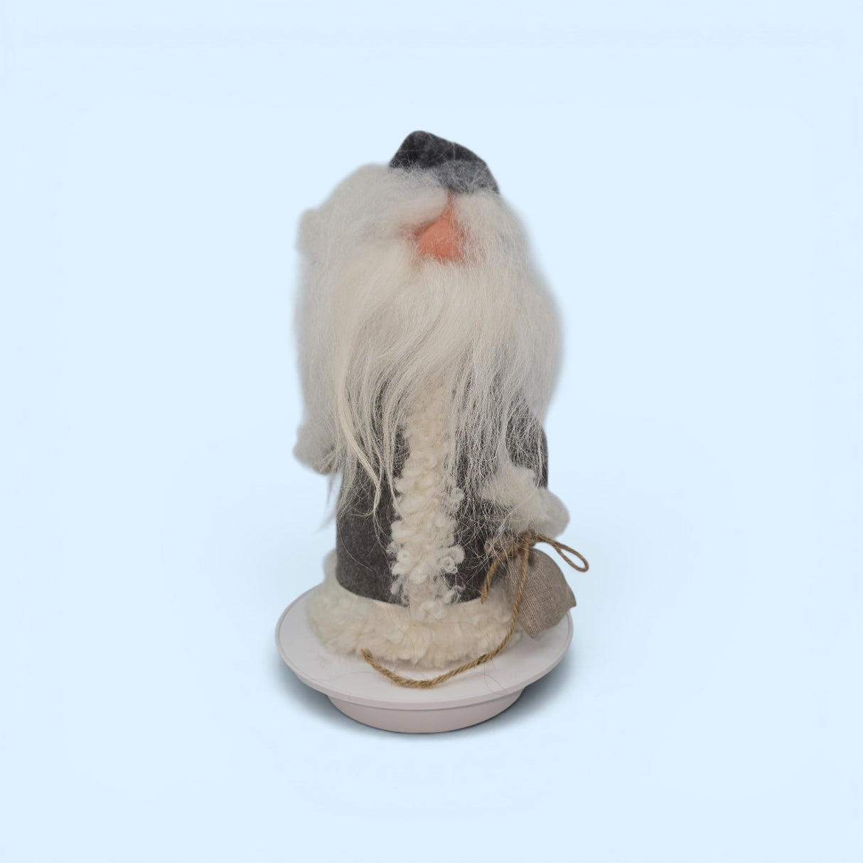 A handmade Swedish gnome figurine, "Tomte with Robe" and Burlap Bag by Gumselids of Sweden, stands 12 inches tall on a wood base. Featuring a long white beard, gray hat, and coat, this charming piece by Talla Imports is inspired by Scandinavian folklore decor and brings the warmth of handcrafted wool gnomes to your home. Displayed against a light blue background.
