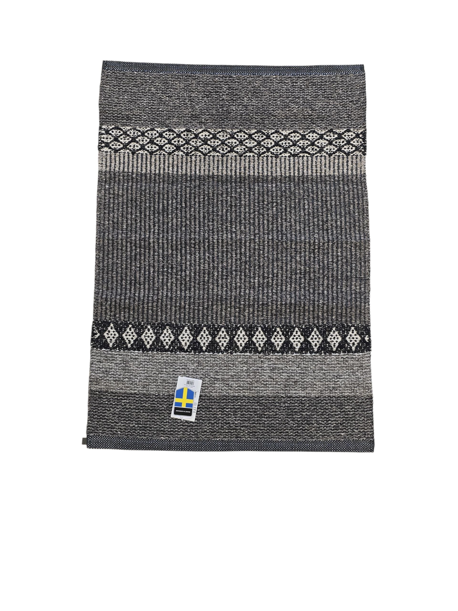A folded gray and black knitted scarf with white geometric patterns and a small Swedish flag tag, inspired by the stylish Forest - Graphite design from the Horredsmattan Cotton/Vinyl Rug collection.